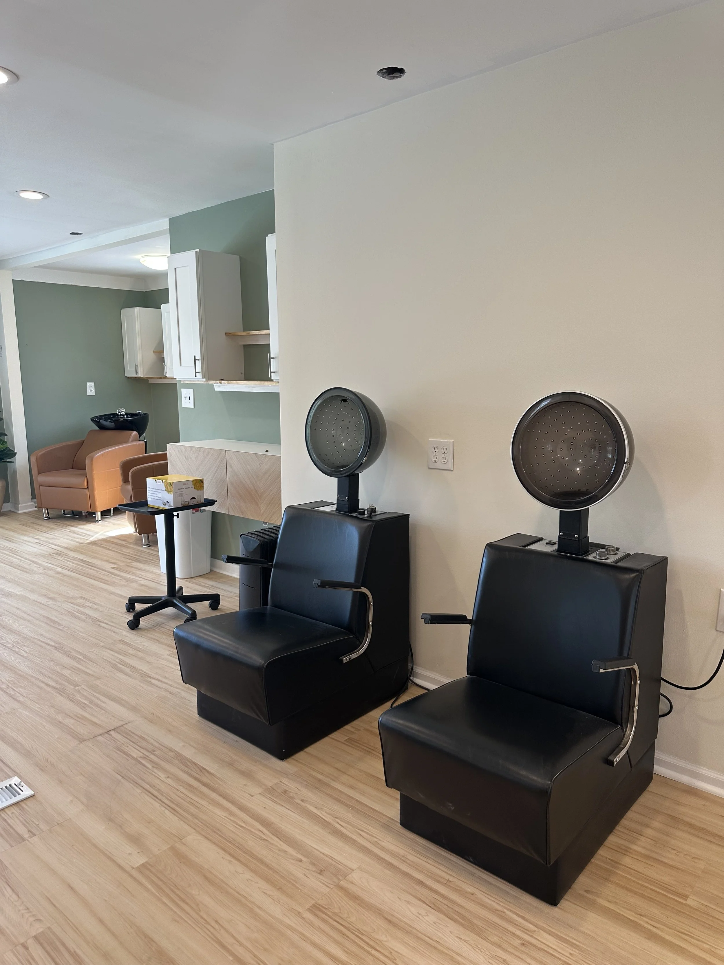 Two black hair washing stations with chairs and dryers in a salon, with modern decor and wooden floors.