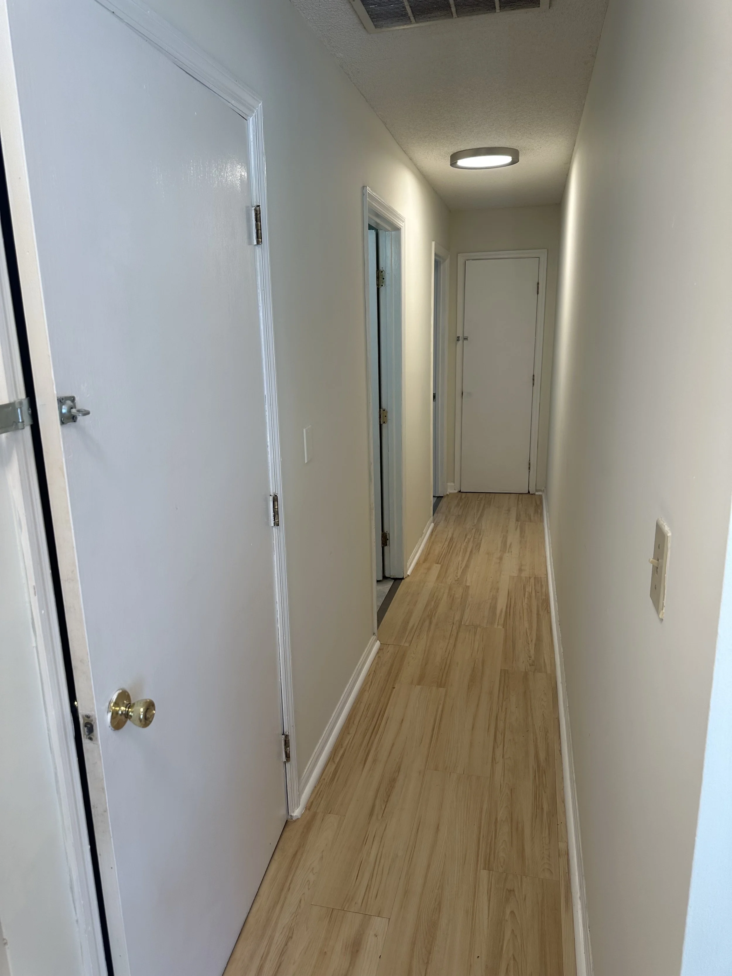 Empty hallway with beige walls, wood flooring, and white doors.