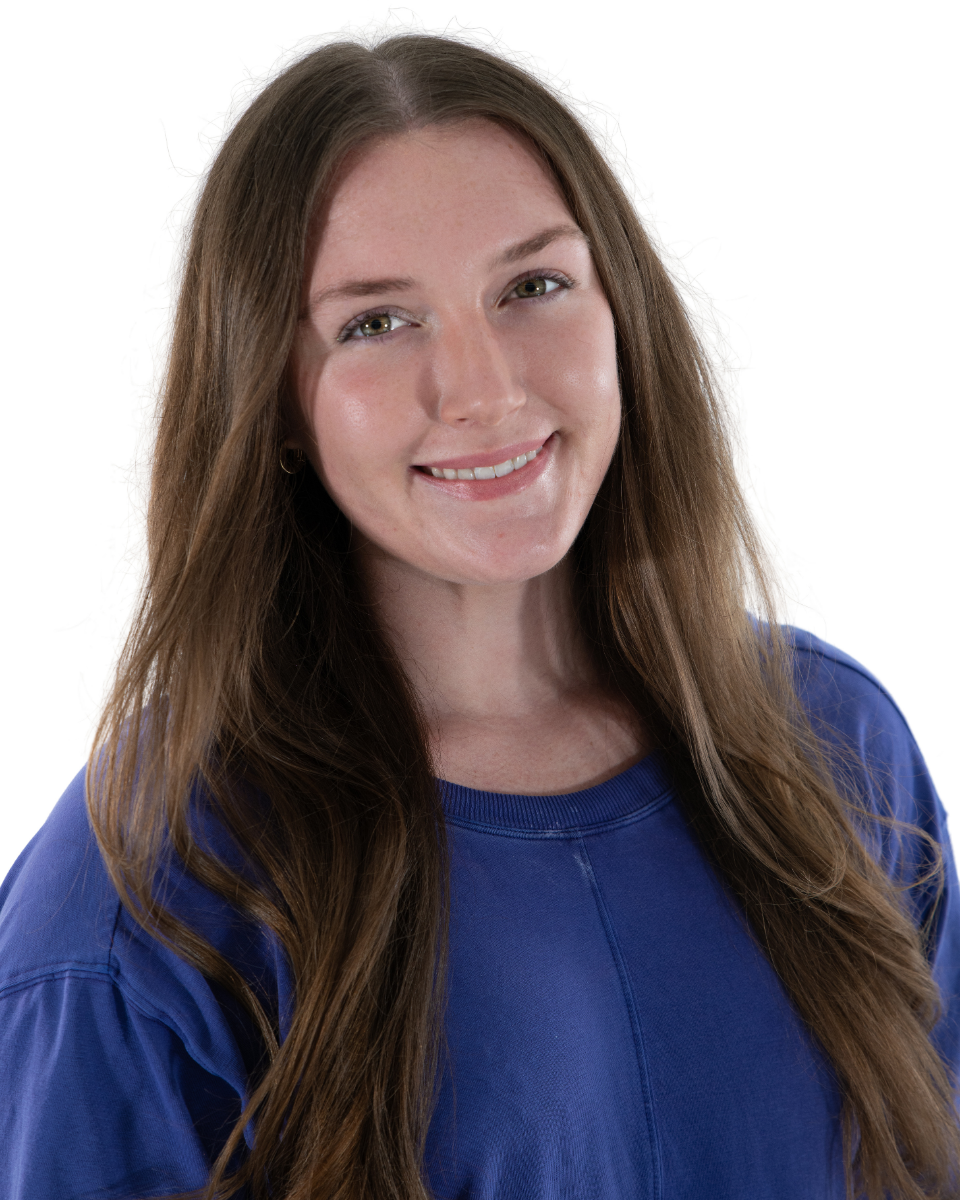 A young woman with long brown hair, smiling, wearing a blue top, against a white background.