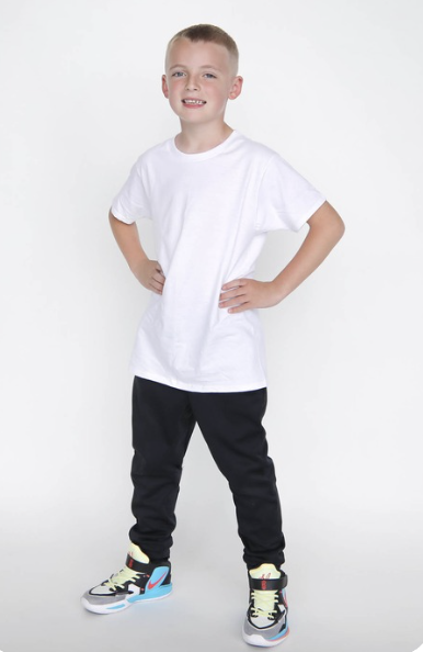 Young boy standing confidently with hands on hips, wearing a white t-shirt, black pants, and colorful sneakers, against a white background.