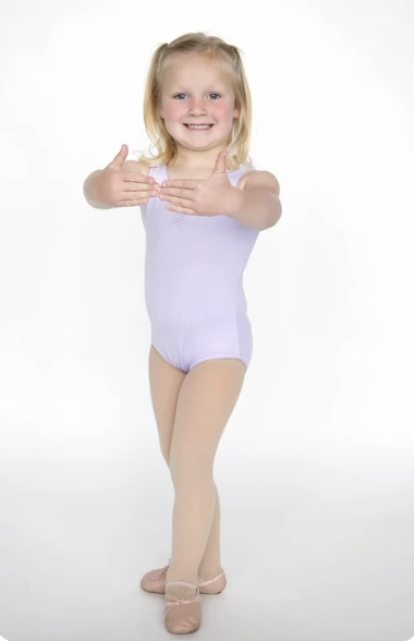 A young girl in a lavender ballet leotard and beige tights standing on a white background, smiling and holding her hands in front of her chest.