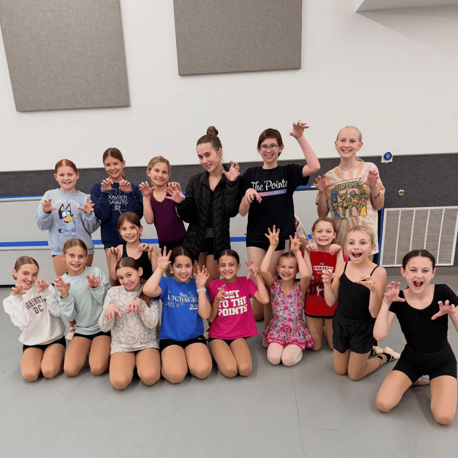 Group of young girls and teenagers posing in a dance studio, making claw hand gestures and smiling.