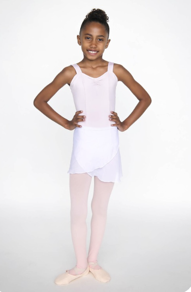 Young girl dressed as a ballerina, wearing a white leotard, tutu, pink tights, and ballet slippers, standing with hands on hips and smiling.
