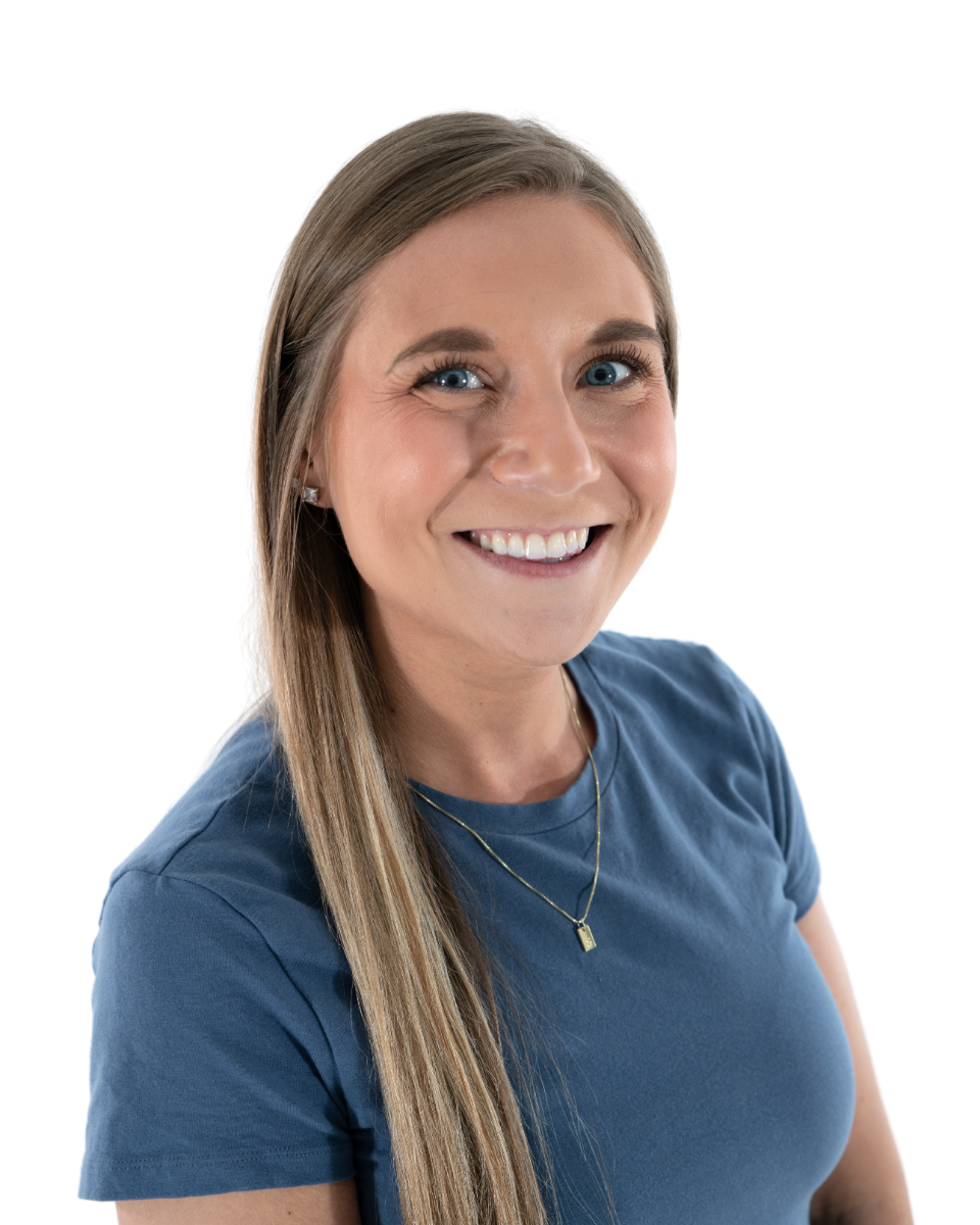 A woman with long brown hair, blue eyes, and light skin smiling, wearing a blue t-shirt and a gold necklace, against a white background.
