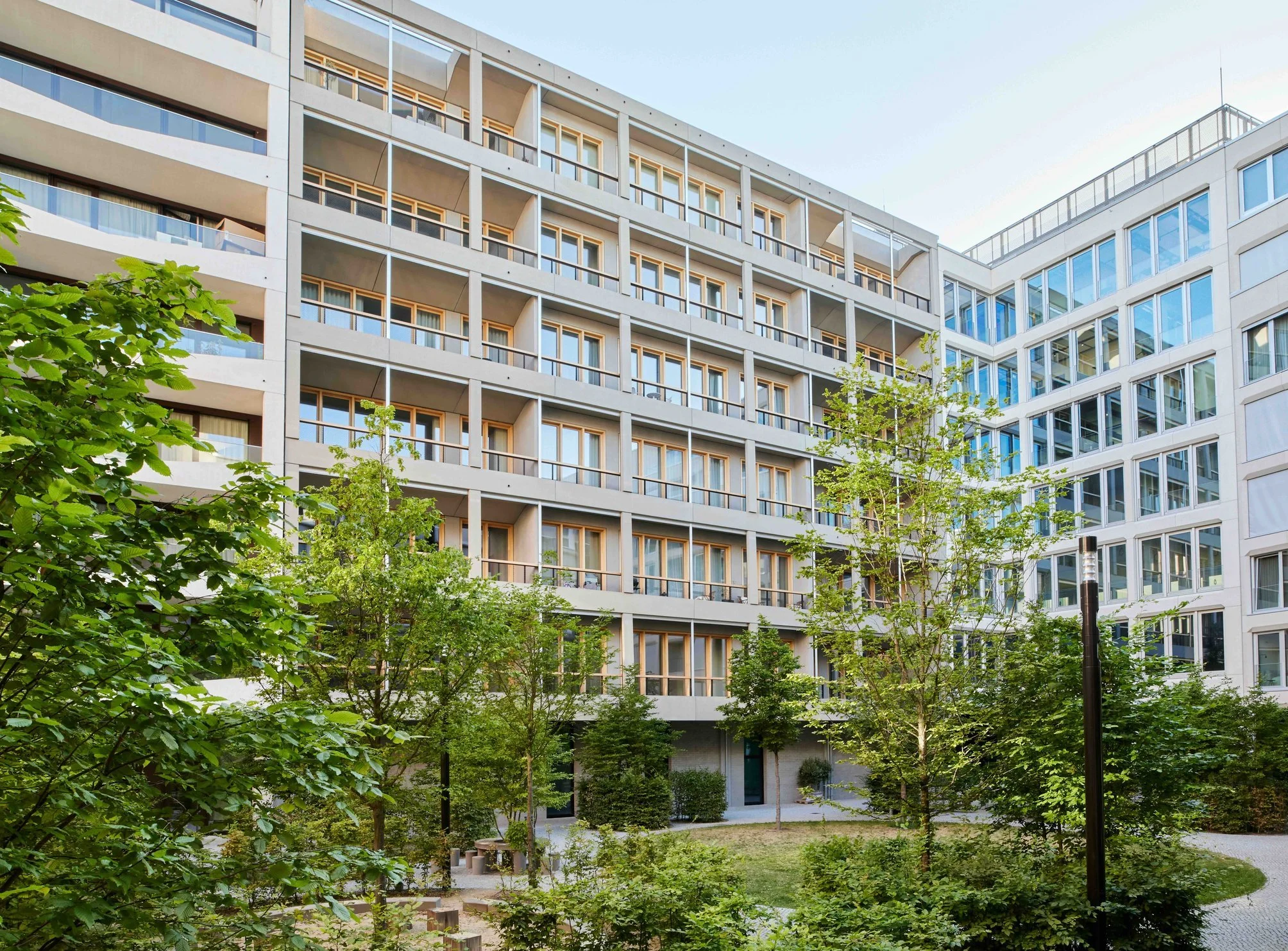 Wohngebäude FRAME mit Balkonen und großen Fenstern, umgeben von grünen Bäumen im Vordergrund.
