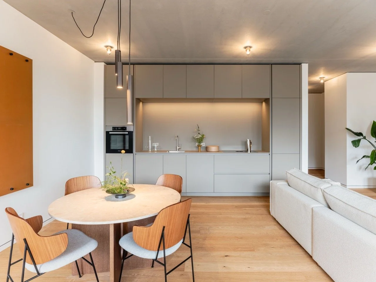 Moderner Küchen- und Wohnraum mit Esstisch, Stühlen, weißen Sofa und minimalistischer Küche