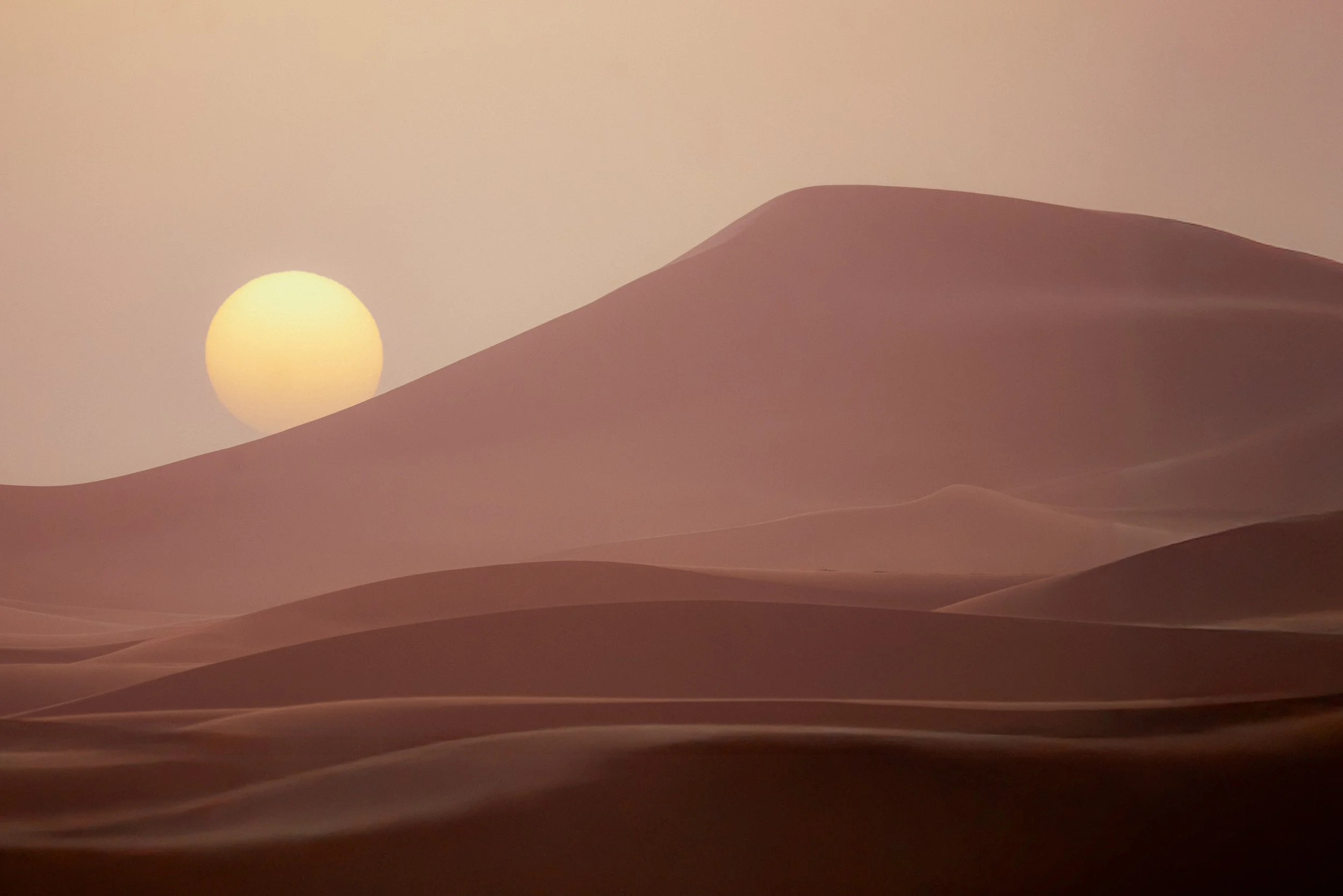 Atardecer en un desierto con dunas y un sol amarillo en el horizonte.