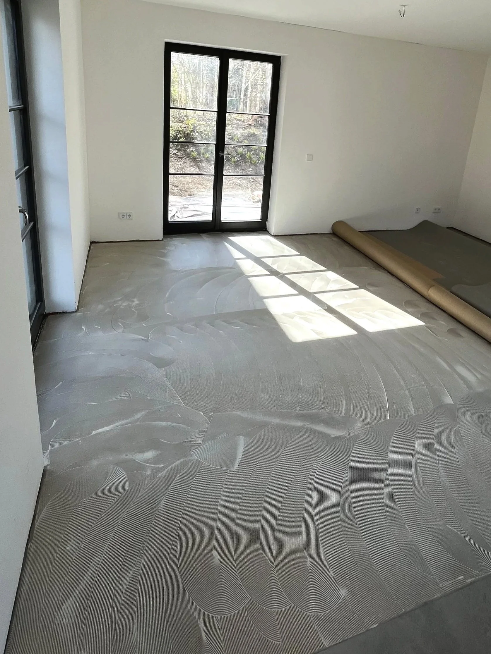Ein Raum mit einem dunklen Doppeltür-Fenster, weiß gestrichenen Wänden und einem neu verlegten grauen Teppichboden mit Mustern.