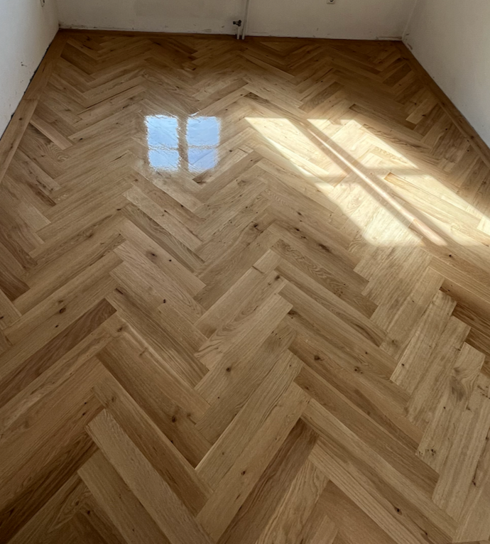 Ein fertig verlegter Holzboden in einem Raum mit natürlicher Holzmaserung und Lichtreflexionen.