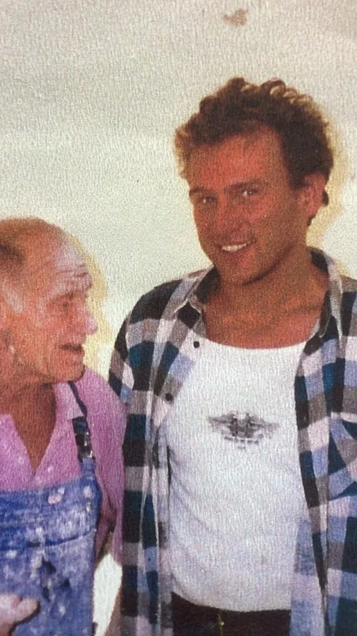 Ein älterer Mann und ein jüngerer Mann stehen nebeneinander und lächeln, die Szene wirkt freundlich und entspannt.