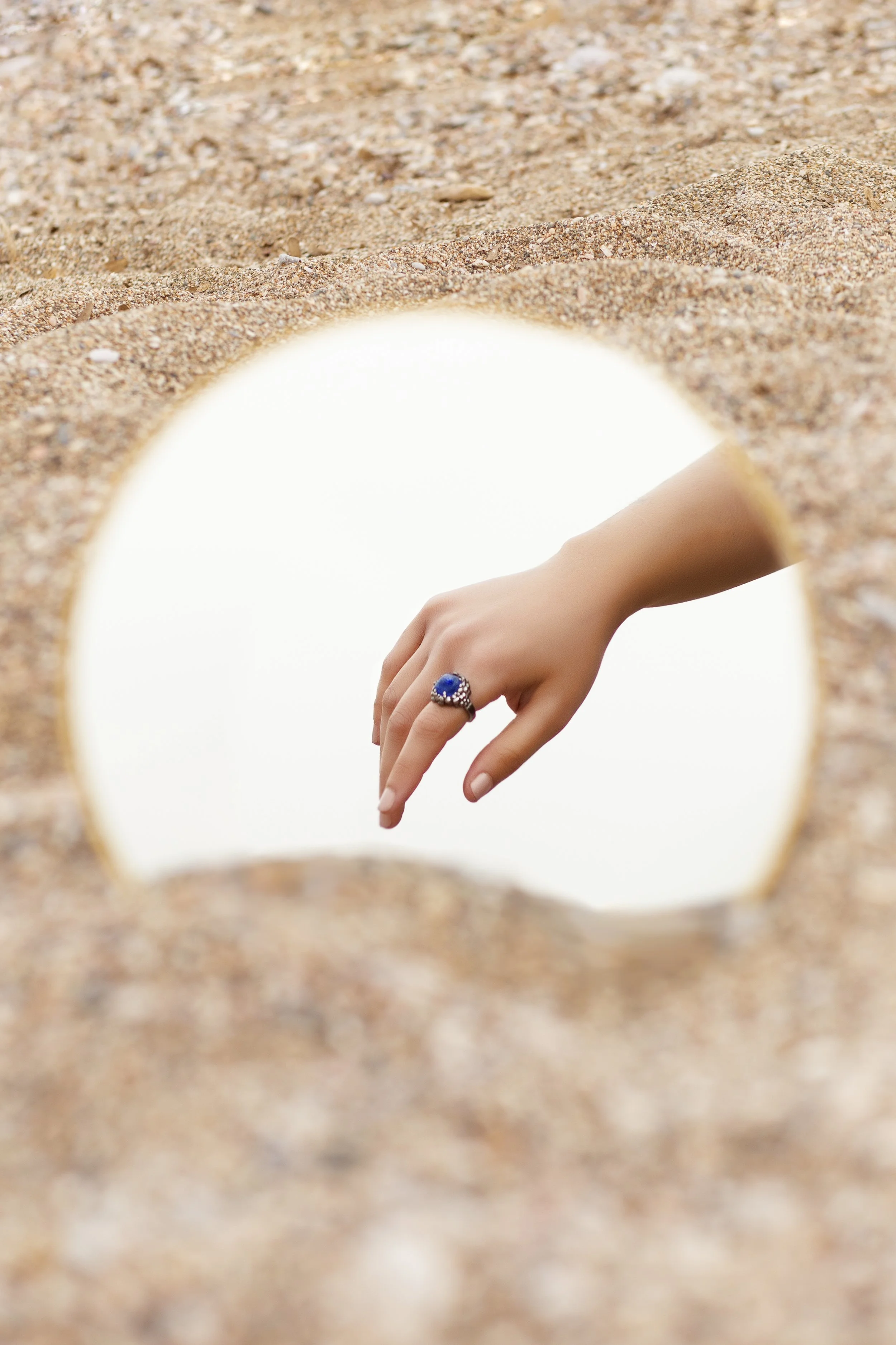 Sterling silver ring with Kyanite blue stone worn on hand, reflected in mirror placed on sand