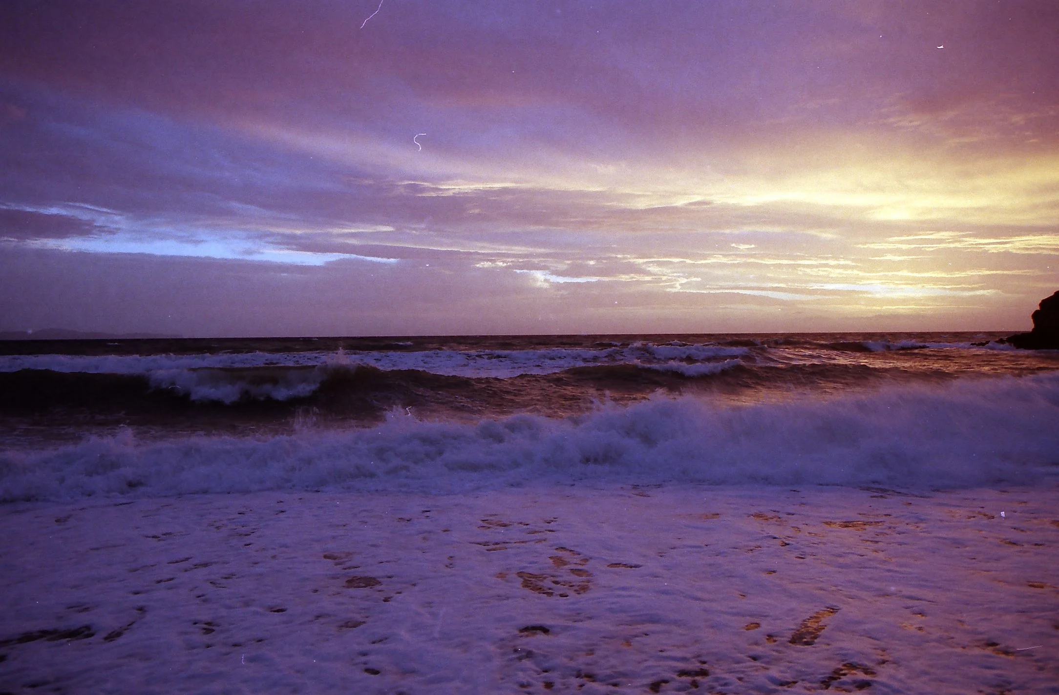 Sunset over a beach with waves crashing and cloudy sky.