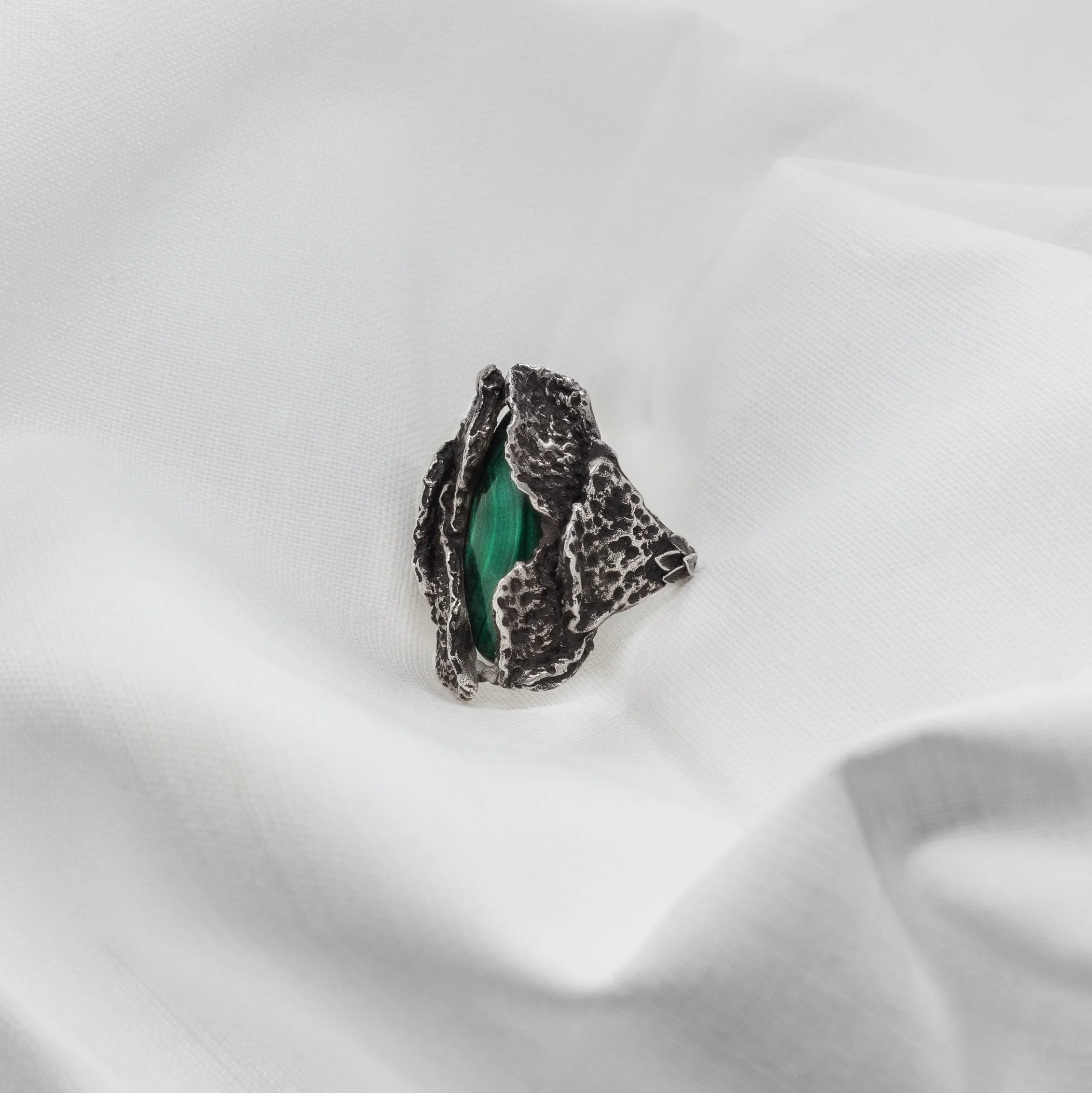 Handmade silver ring with malachite stone set between textured rind-like forms, sculptural organic jewelry by Cadera Jewelry