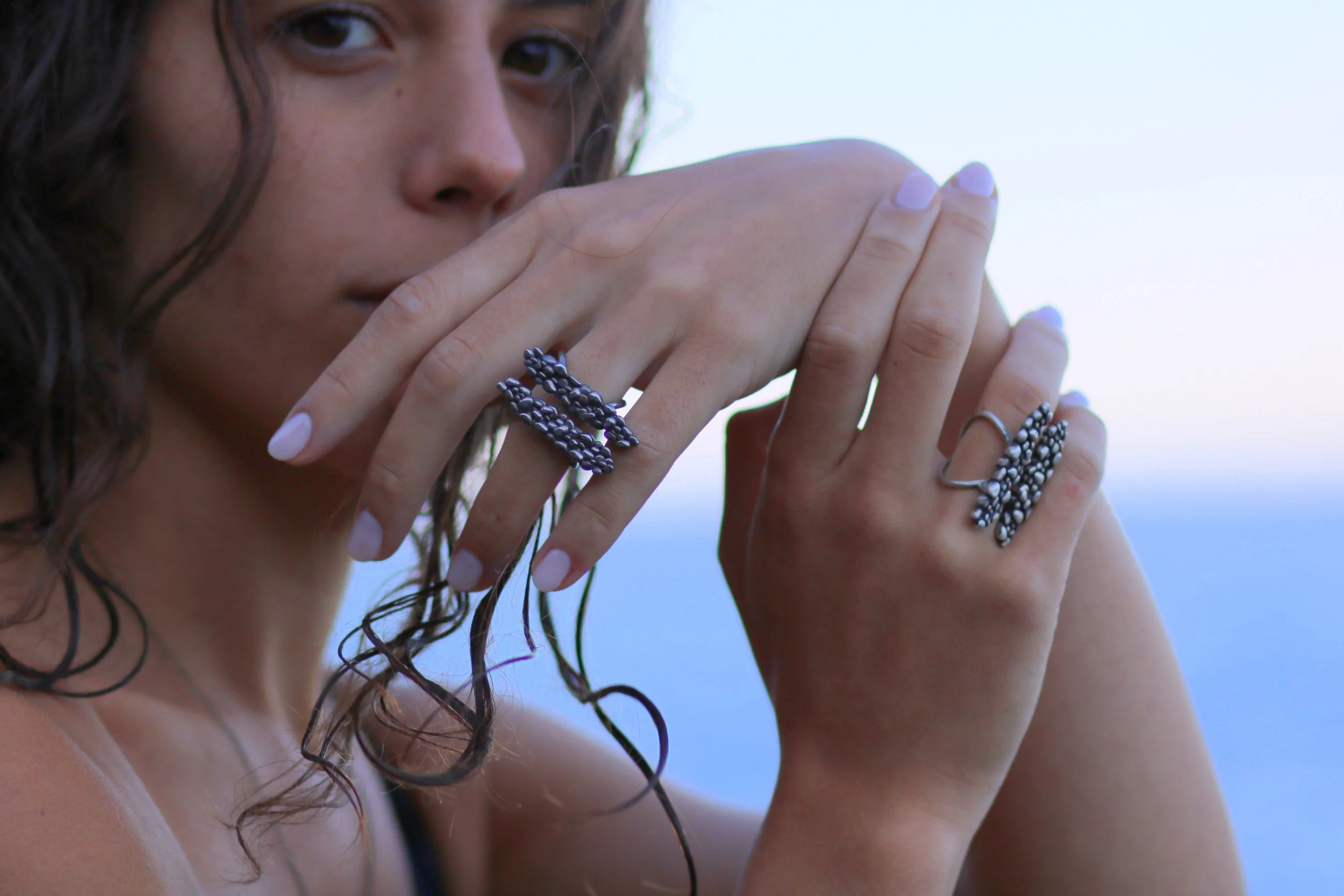 Model wearing handmade silver pebble cluster rings inspired by coastal stones, sculptural jewelry by Cadera Jewelry