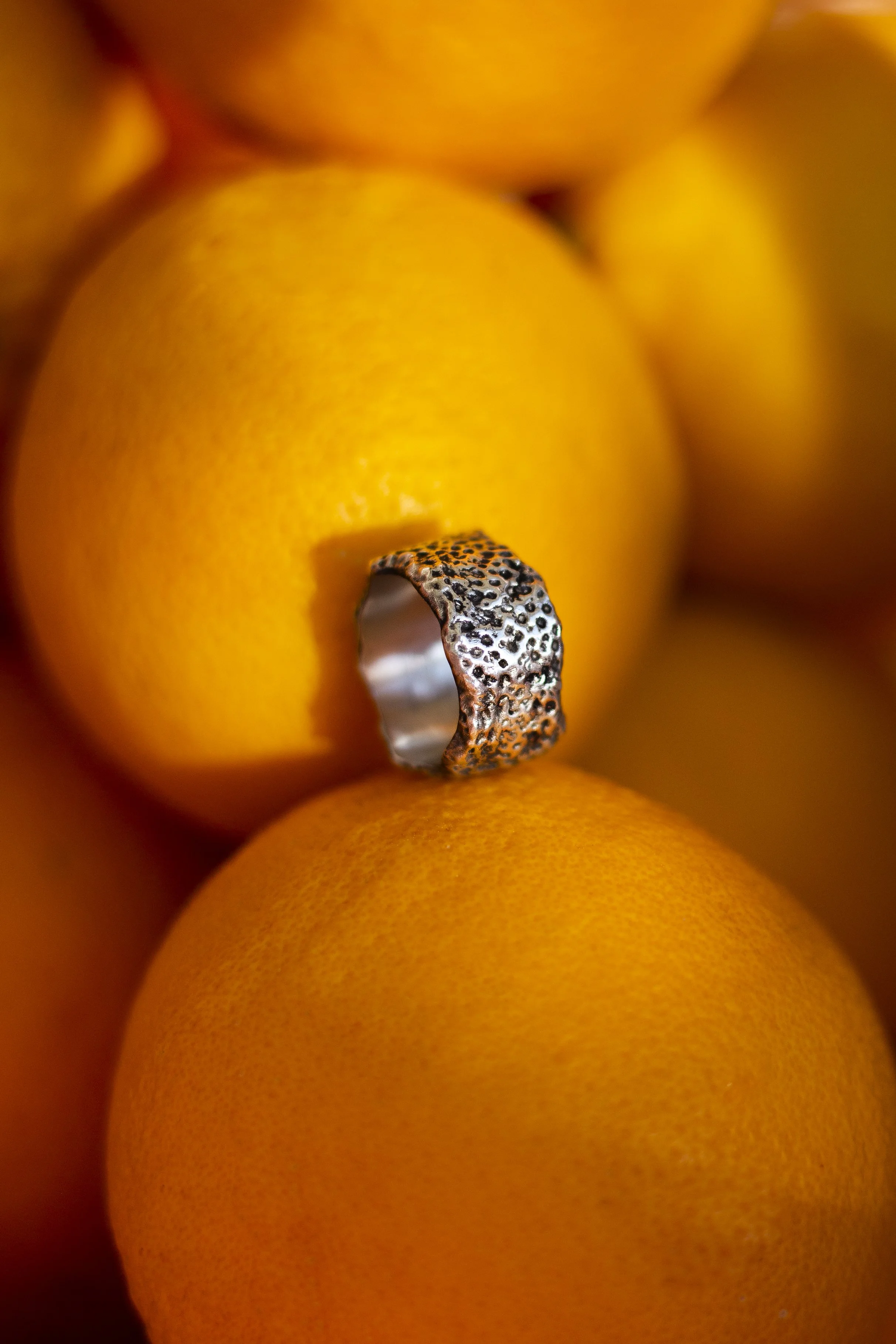 Sterling silver ring with textured surface inspired by tangerine peel, placed on fresh oranges