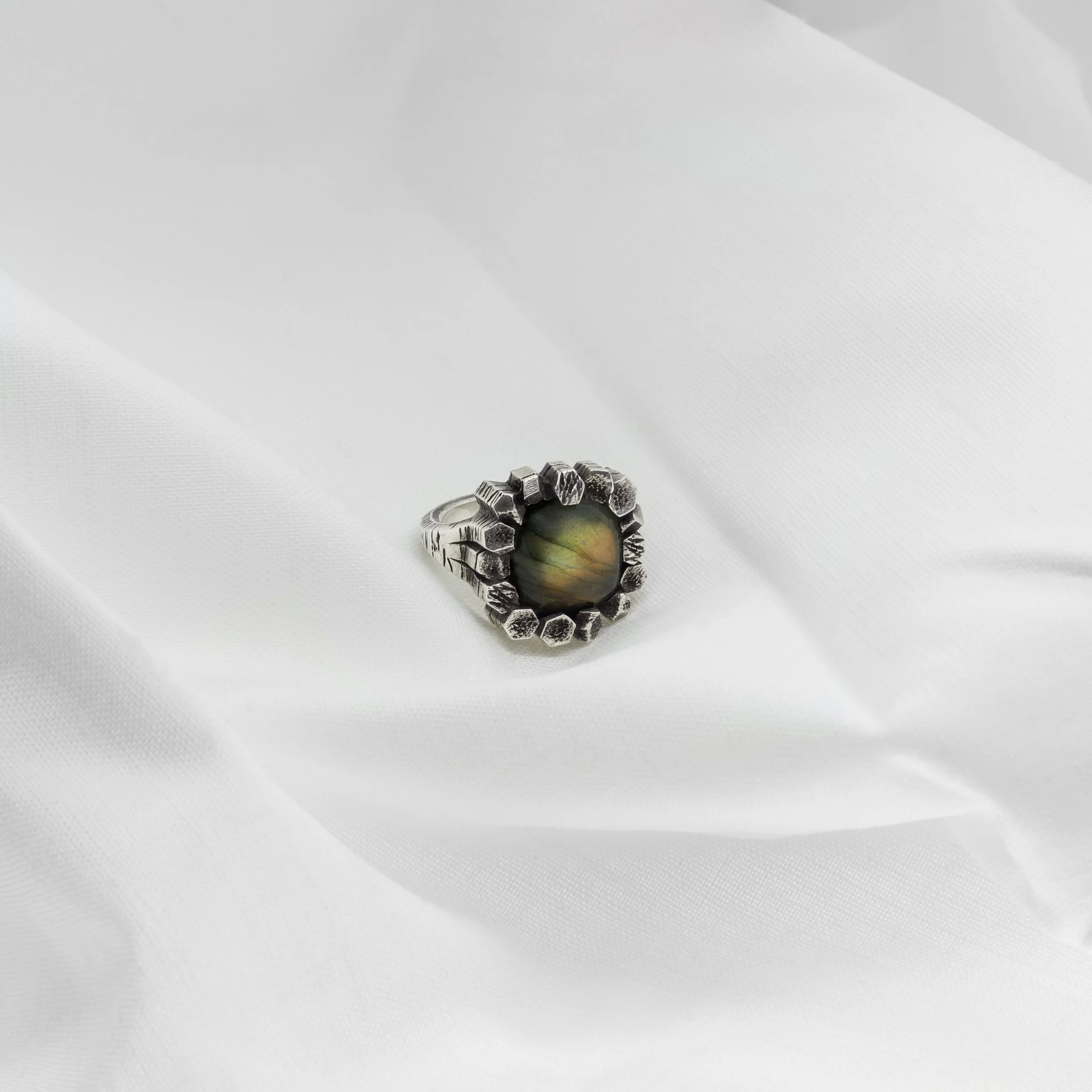 Sterling silver labradorite basalt ring featuring a yellow and green iridescent stone with shifting tones, set within a textured basalt-like sculptural form inspired by volcanic coastal landscapes, design by Cadera Jewelry