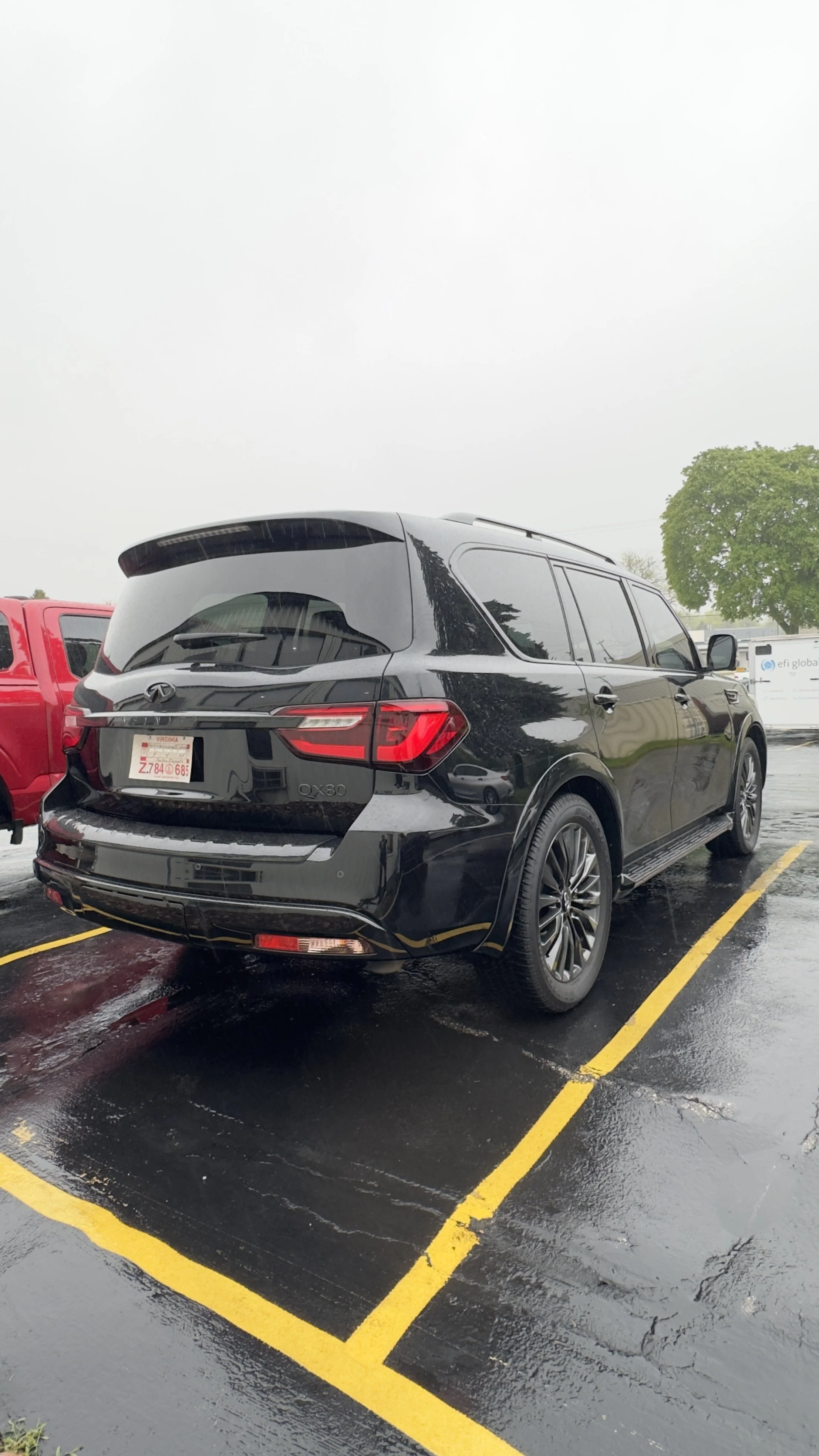 A black Infiniti QX80 SUV parked in a parking lot on a rainy day.