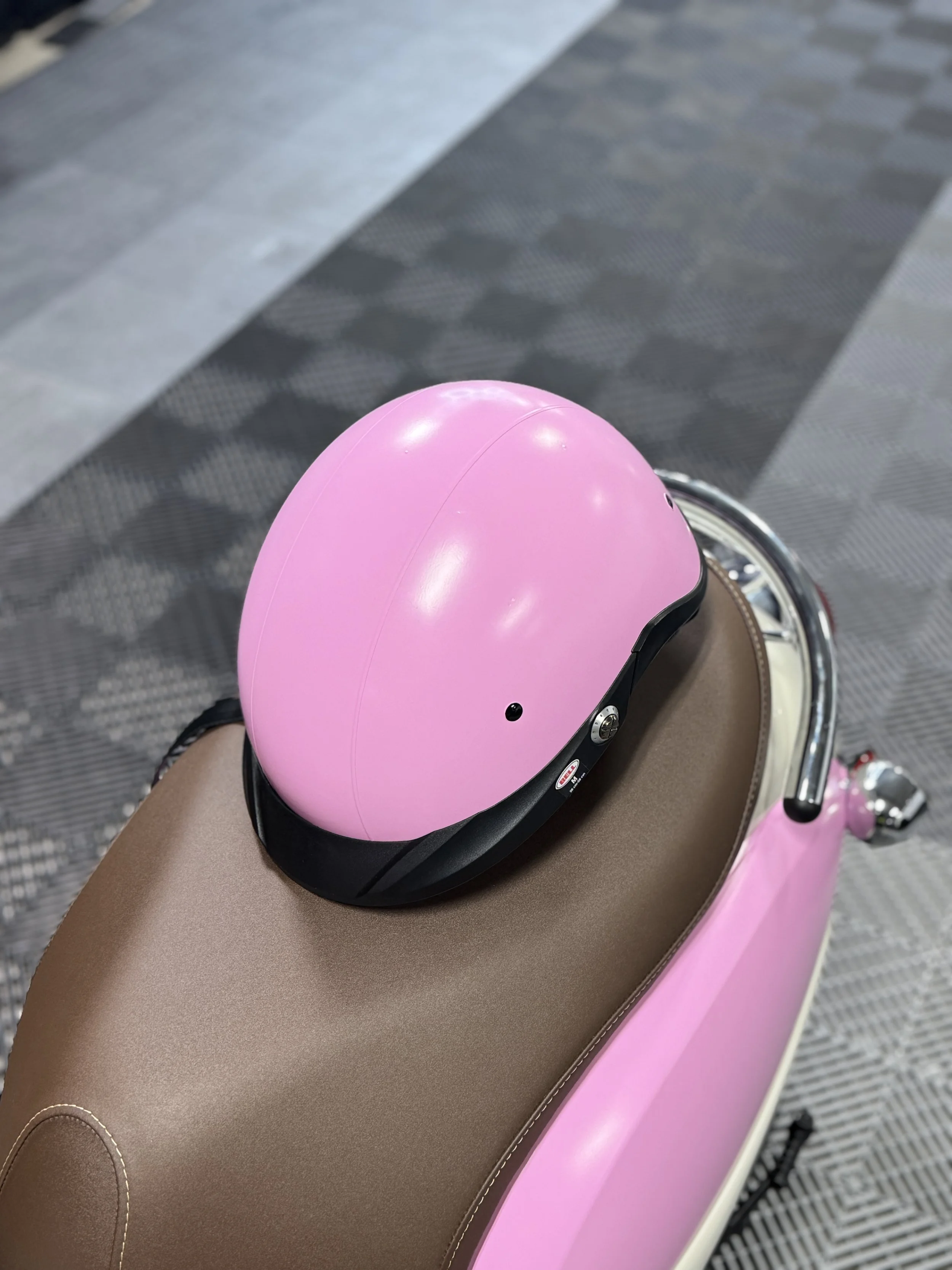 Pink motorcycle helmet resting on a tan seat on a pink scooter.