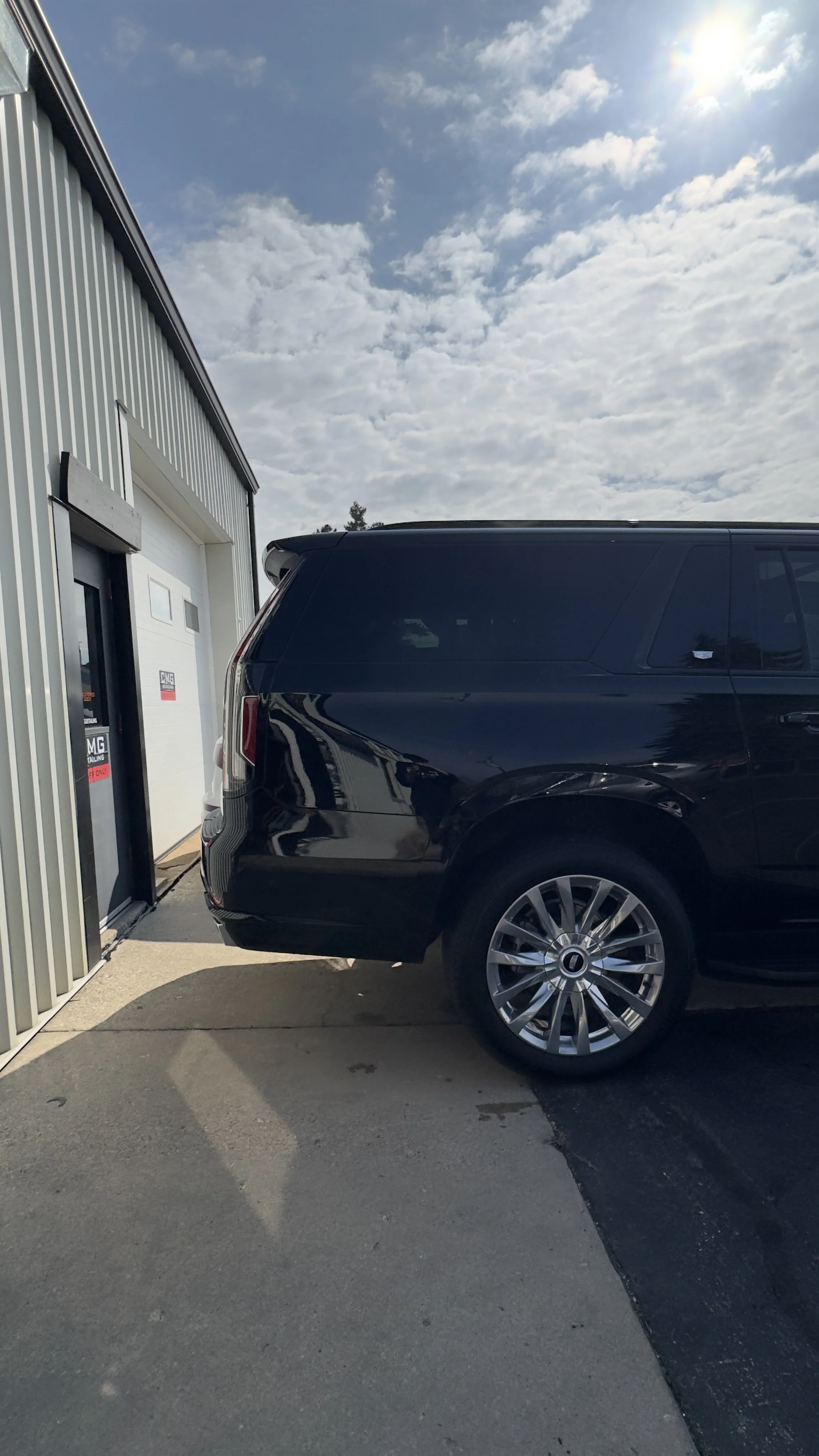 Front of a black SUV parked in front of a garage door at a service shop on a day with partly cloudy skies.