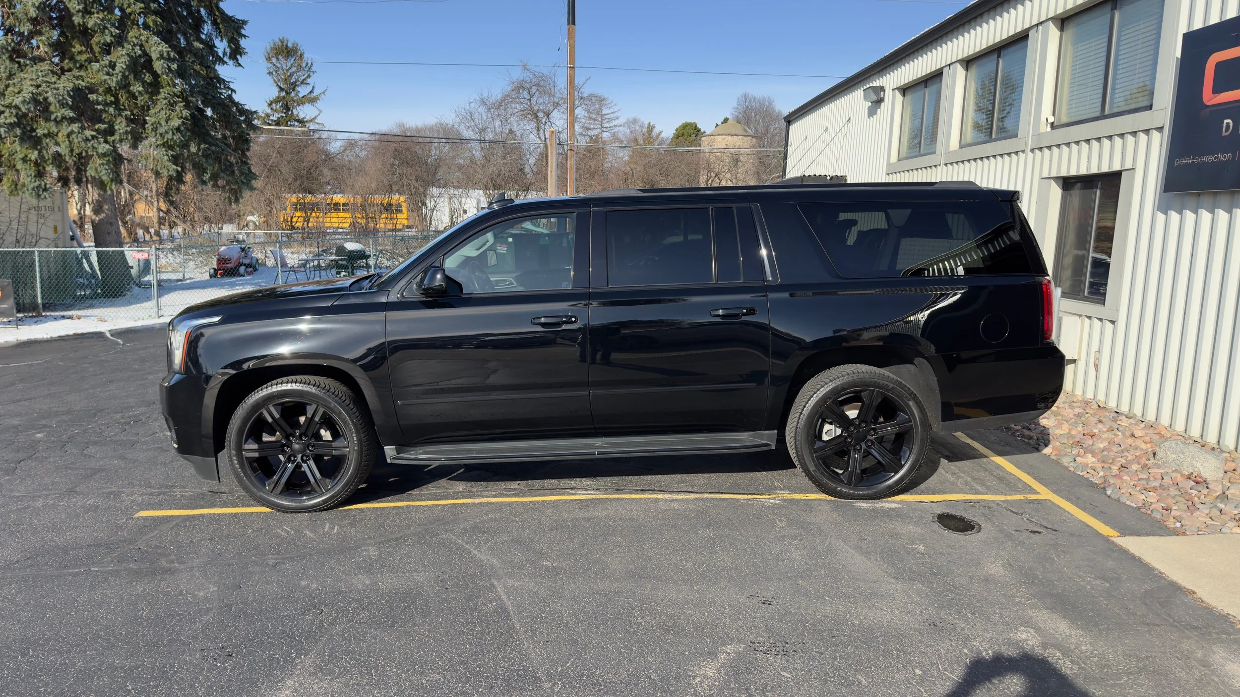 Black SUV parked in a parking lot near a building with a sign that says "point correction". The parking lot has some snow and trees in the background.