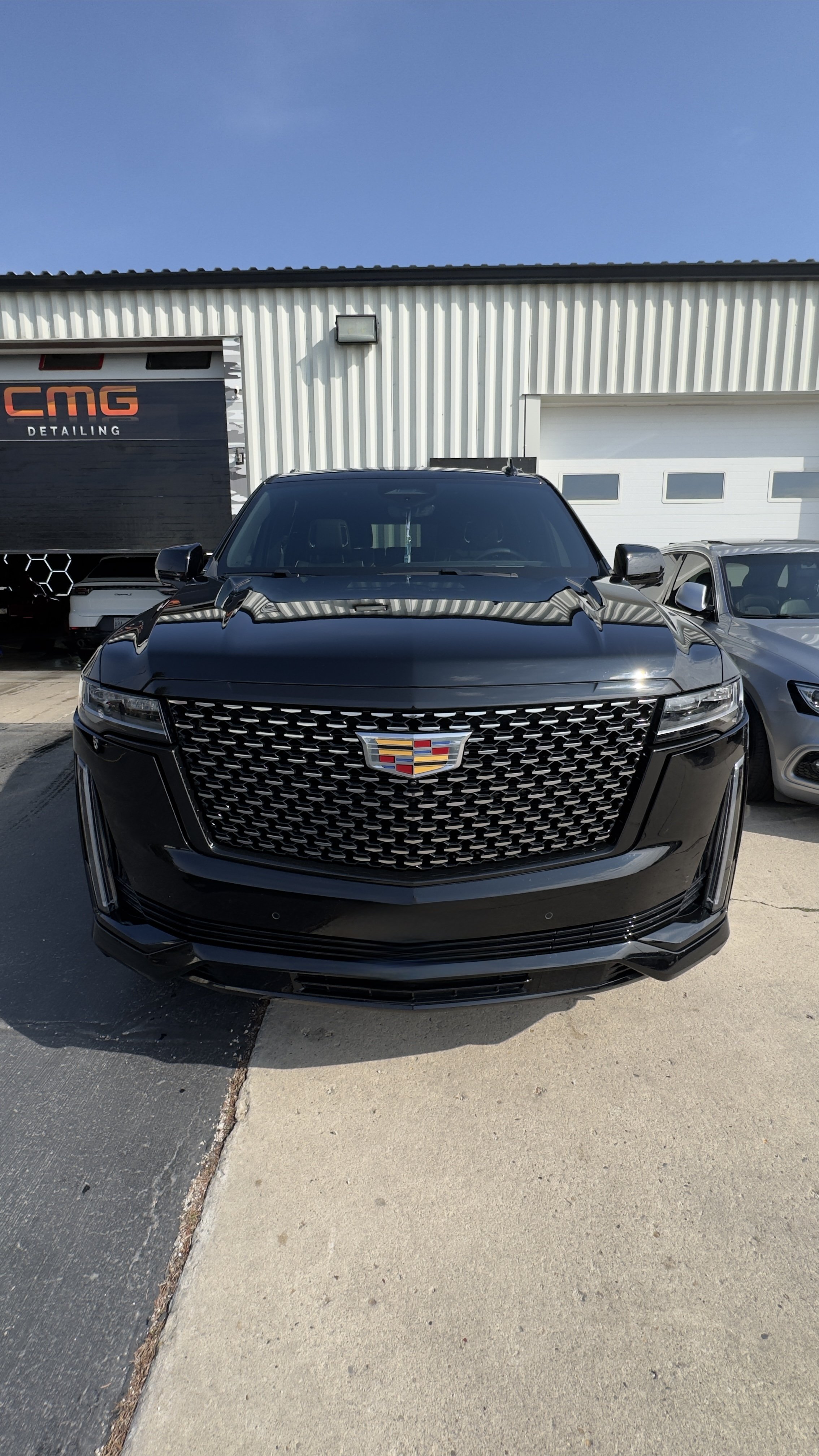 Black Cadillac SUV parked outside a detailing shop with a white building and garage door in the background.