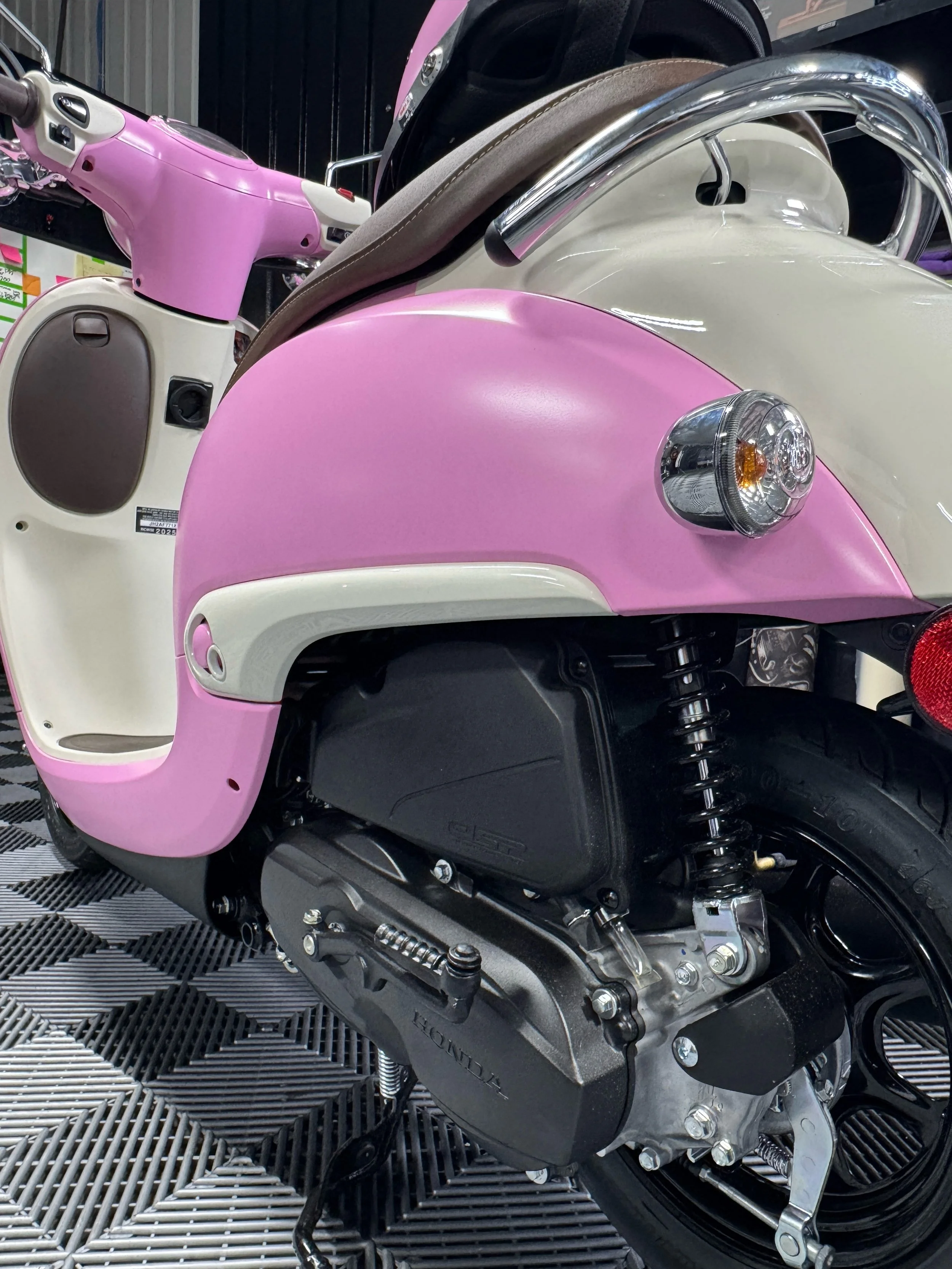 Close-up of a pink and white scooter showing the front fender, headlight, and engine components.