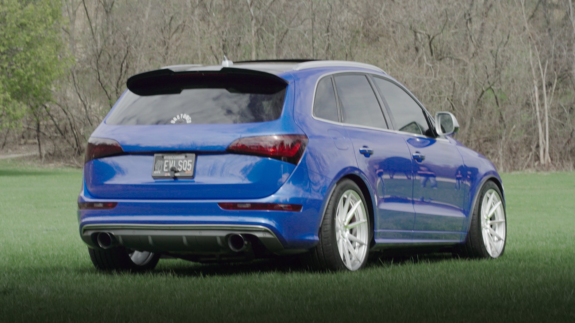 Blue station wagon parked on grass field with trees in the background.