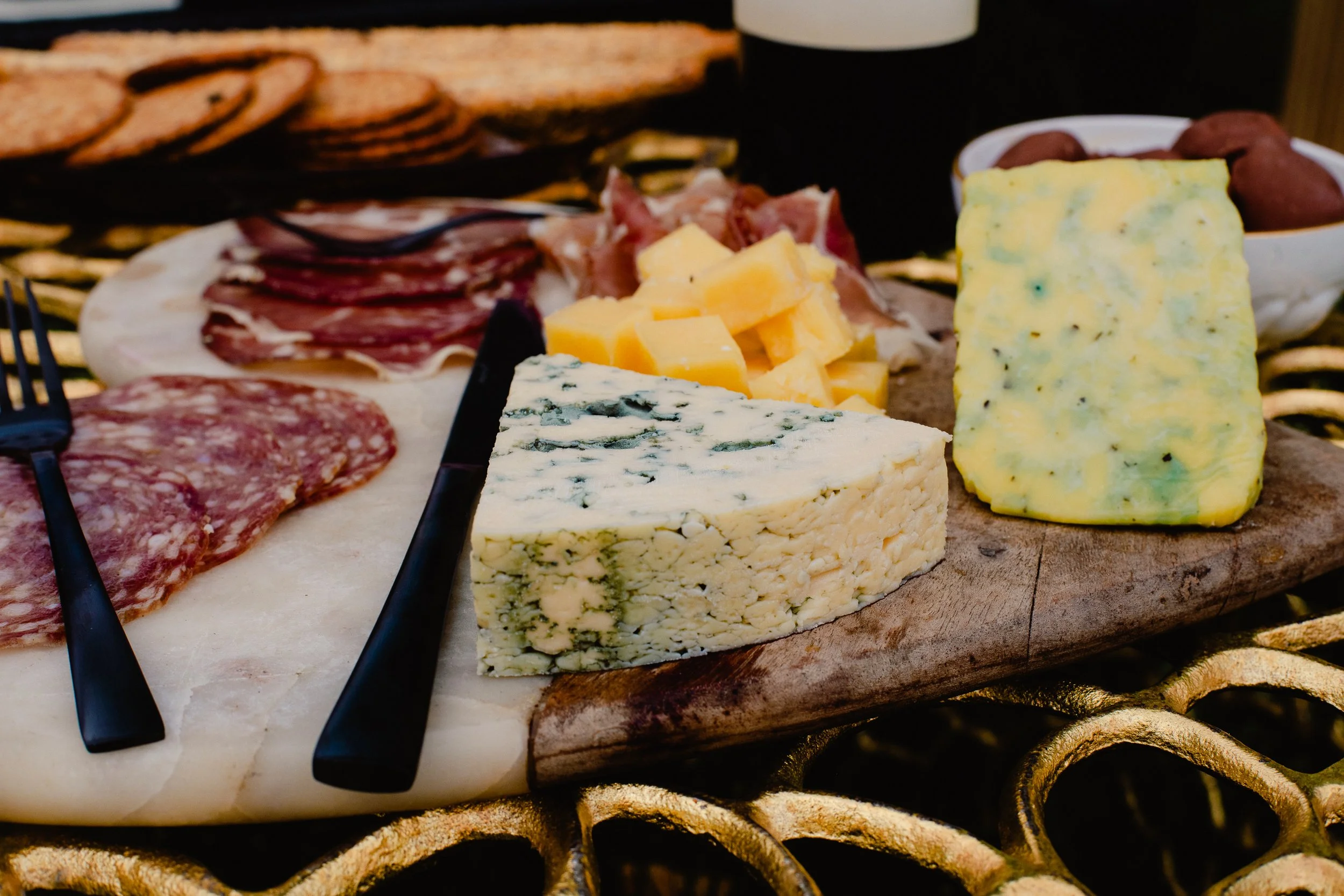 Cheese, meats, and crackers arranged on a wooden serving board, with tongs in the foreground.
