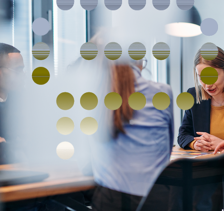 People sitting at a table in a modern office conference room, seen through glass with decorative dots.