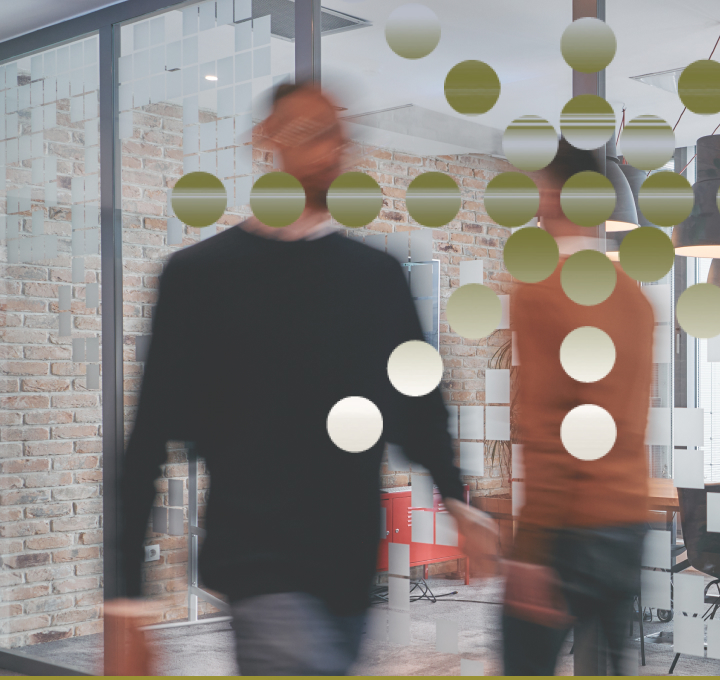 Blurred image of two people walking past glass wall with green and white circular decorations in an office with brick walls and modern furniture.