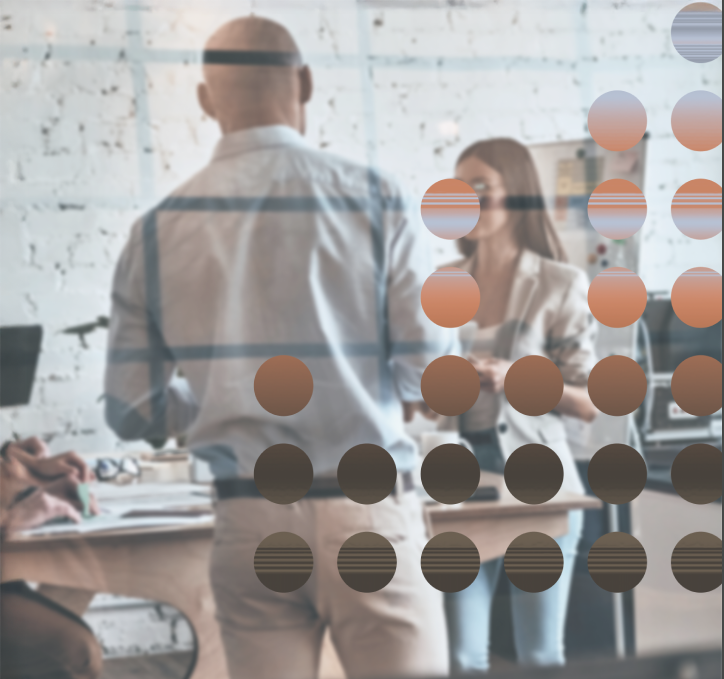 Two people in an office having a discussion, blurred view from behind of a man with glasses and a woman with long hair, behind a glass wall with colorful dots.
