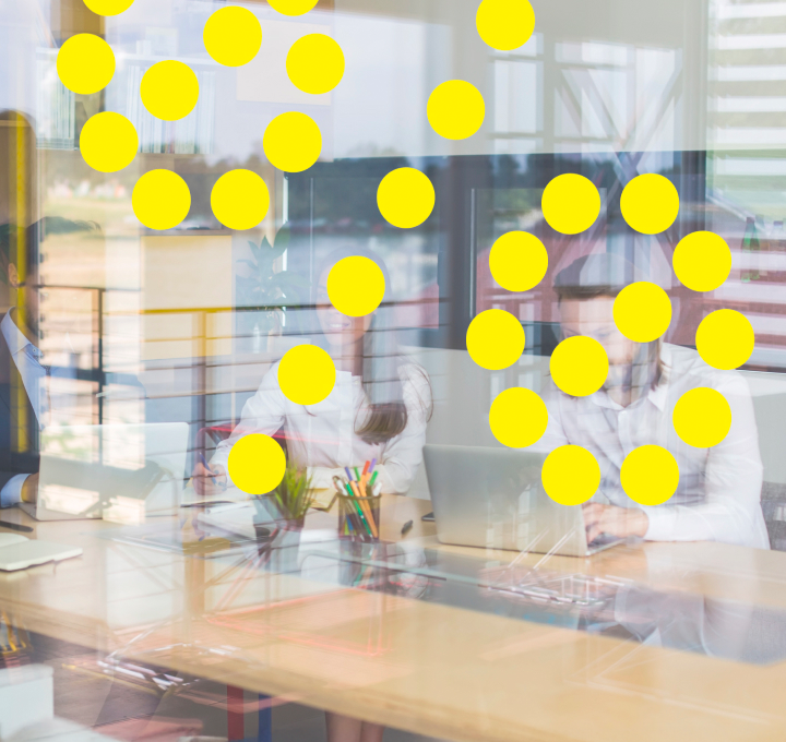 People working in a modern office with large windows, viewed through a glass wall with yellow circular stickers.