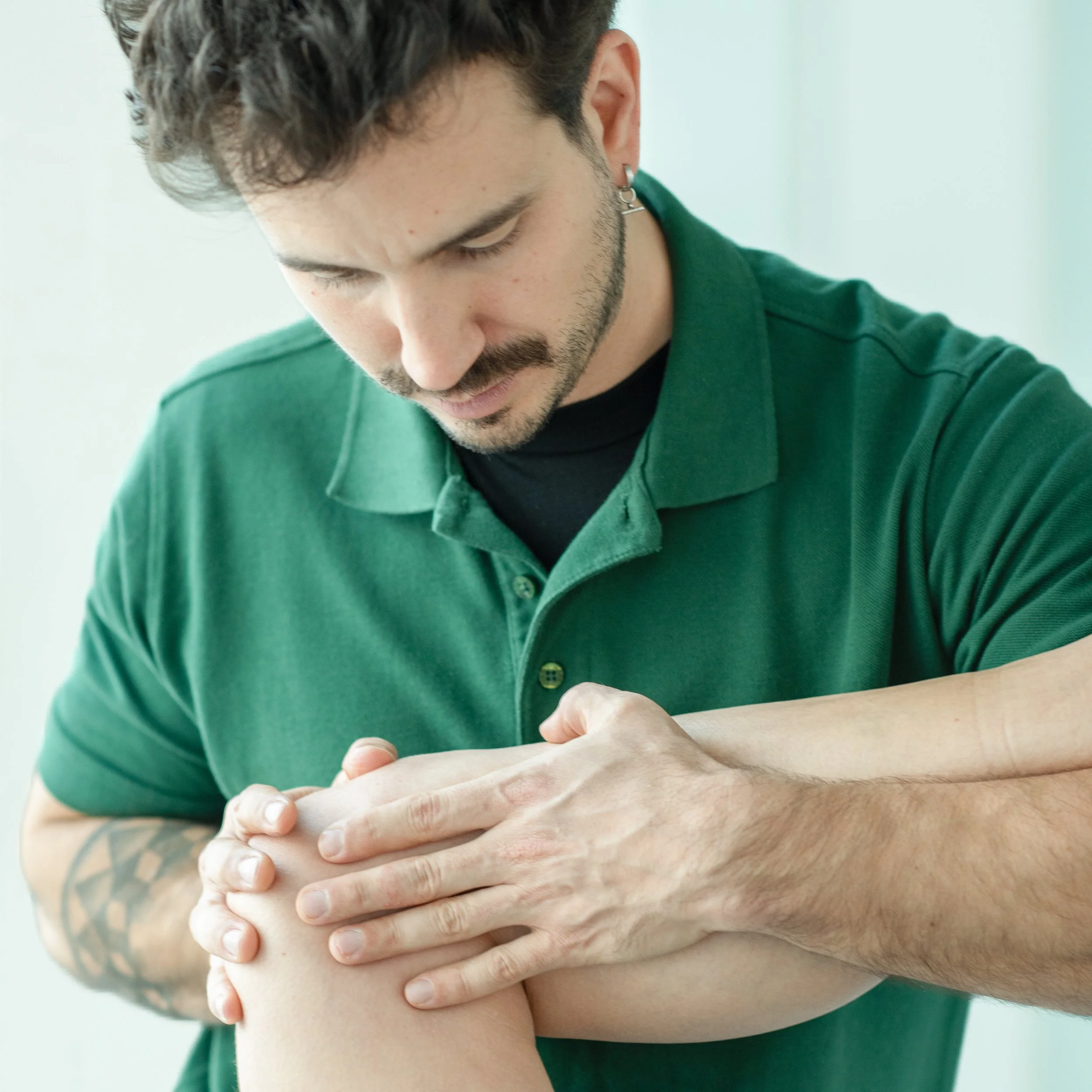 Mann in grüner Poloshirt, der eine Person am Knie behandelt.