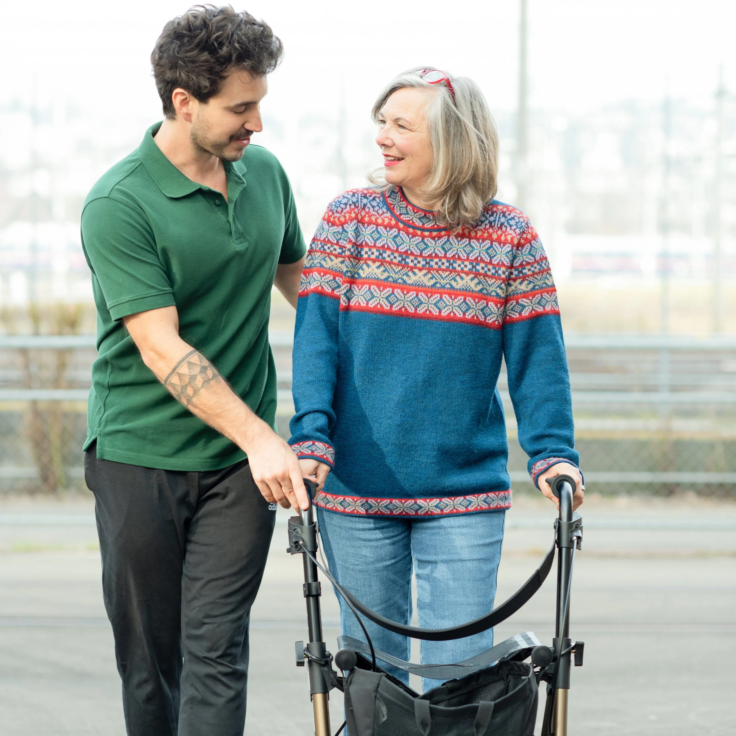 Ein junger Mann hilft einer älteren Frau mit einem Rollator.