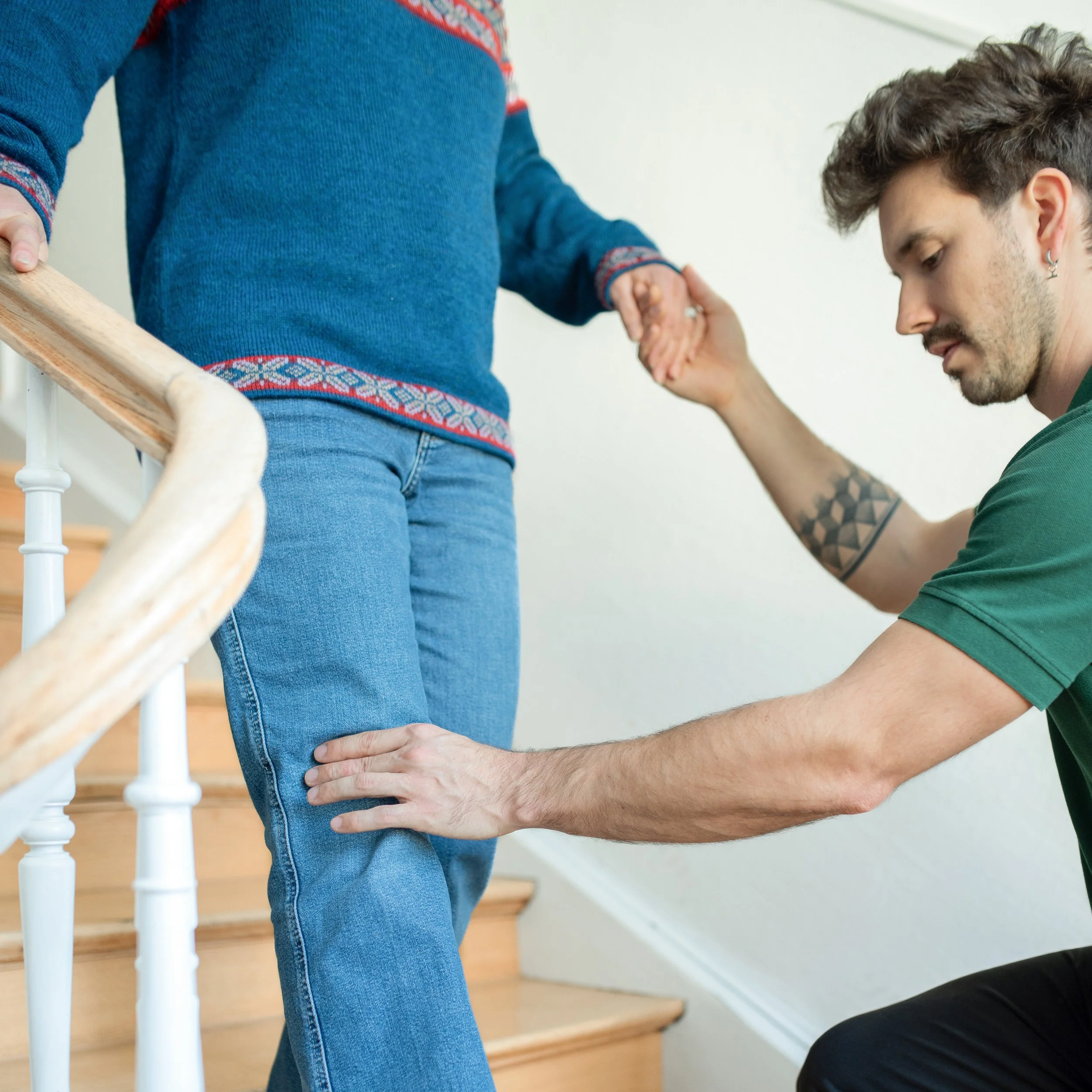 Ein Mann hilft einer Frau beim Treppensteigen, indem er ihre Beine misst oder unterstützt, während sie die Treppe hinaufgeht.