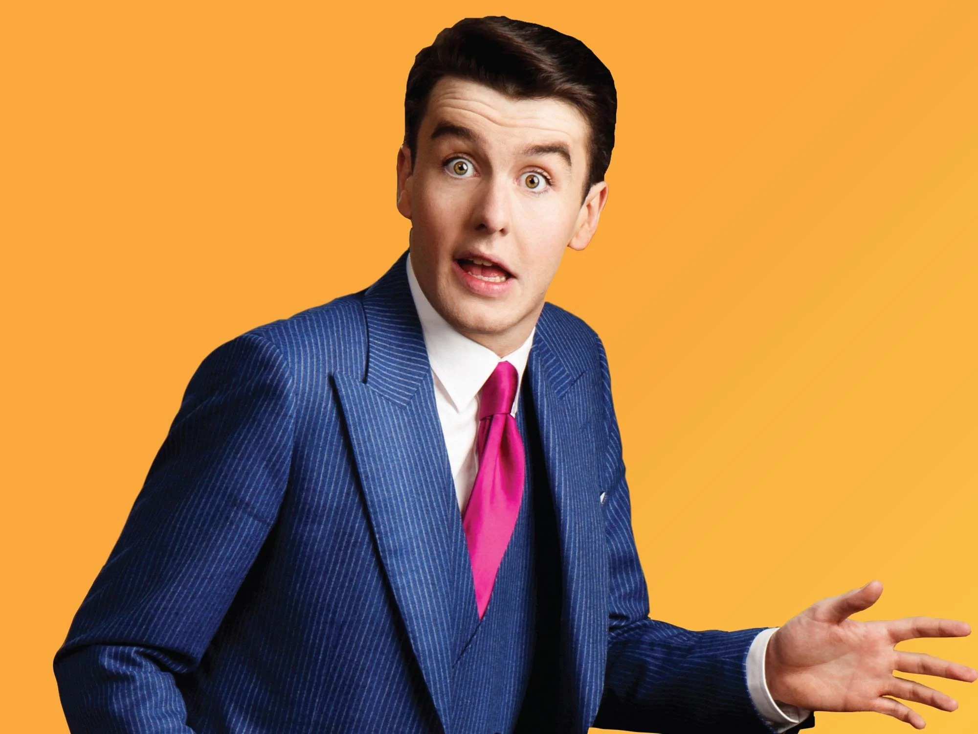A man with dark hair dressed in a blue pinstripe suit, white shirt, and pink tie, making an expressive gesture with his hand against a solid orange background.
