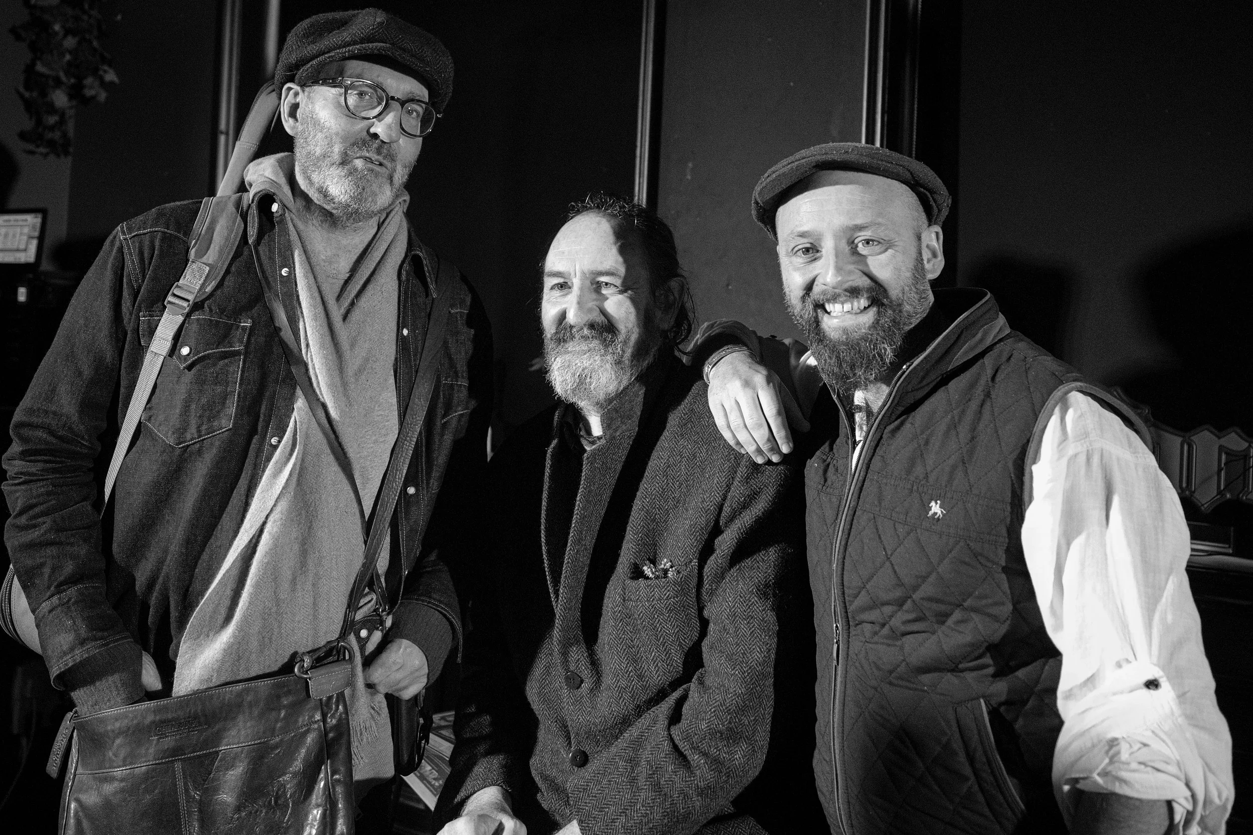 Three smiling men in casual attire posing together inside a building.