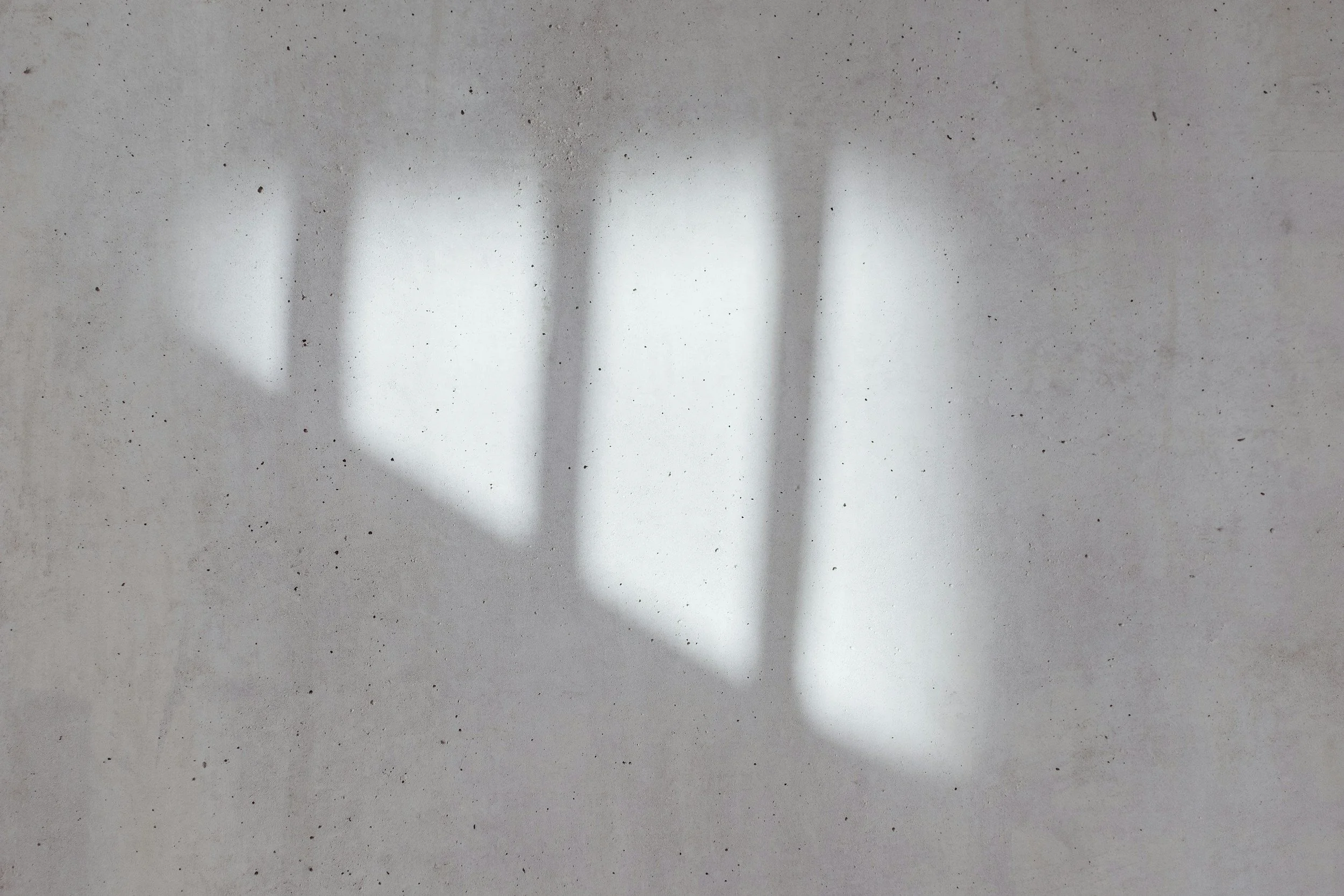Shadow of a staircase and a railing cast on a concrete wall.