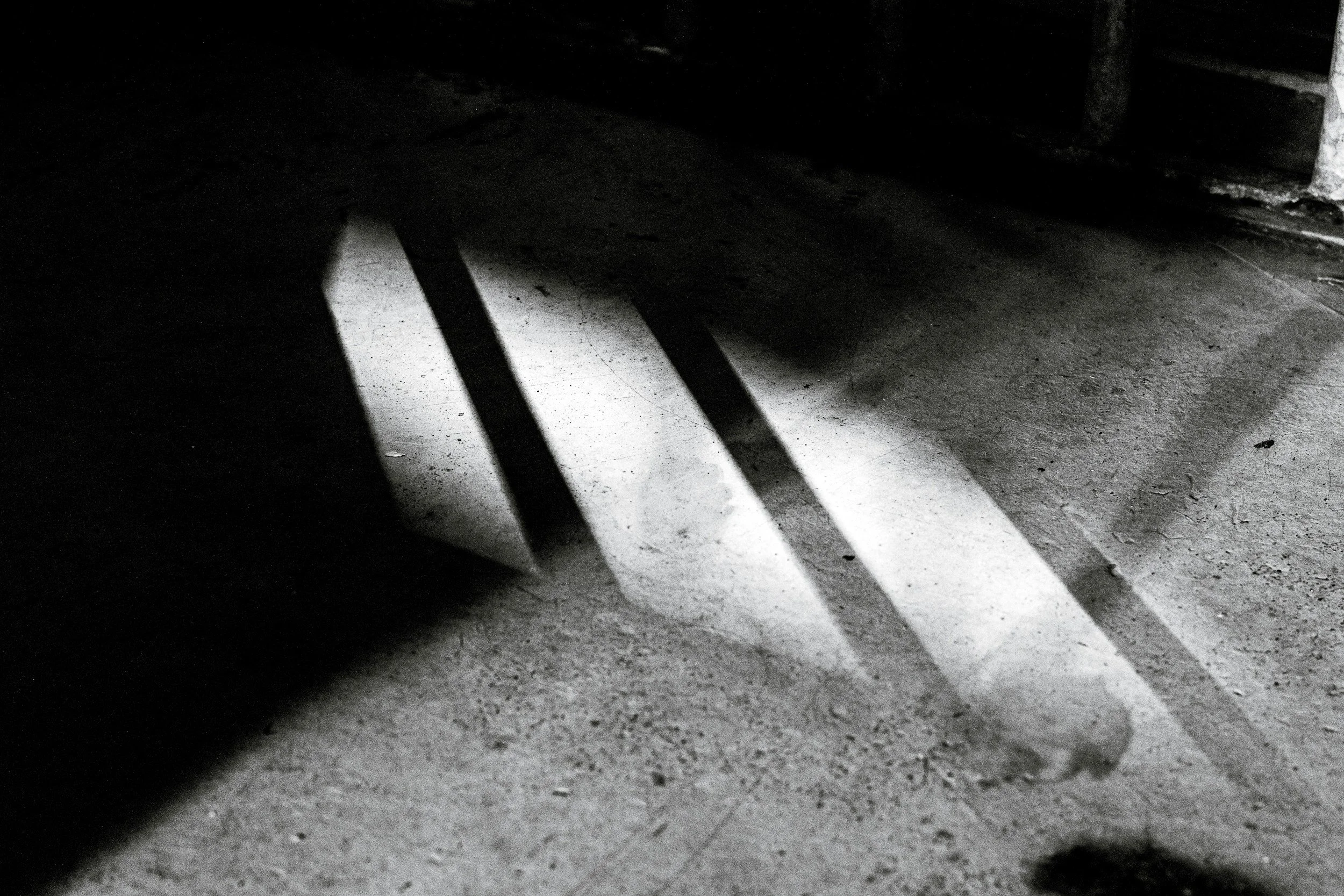 Black and white photo of a table with a drop of water on the surface and white paper underneath, with shadows cast on the floor.