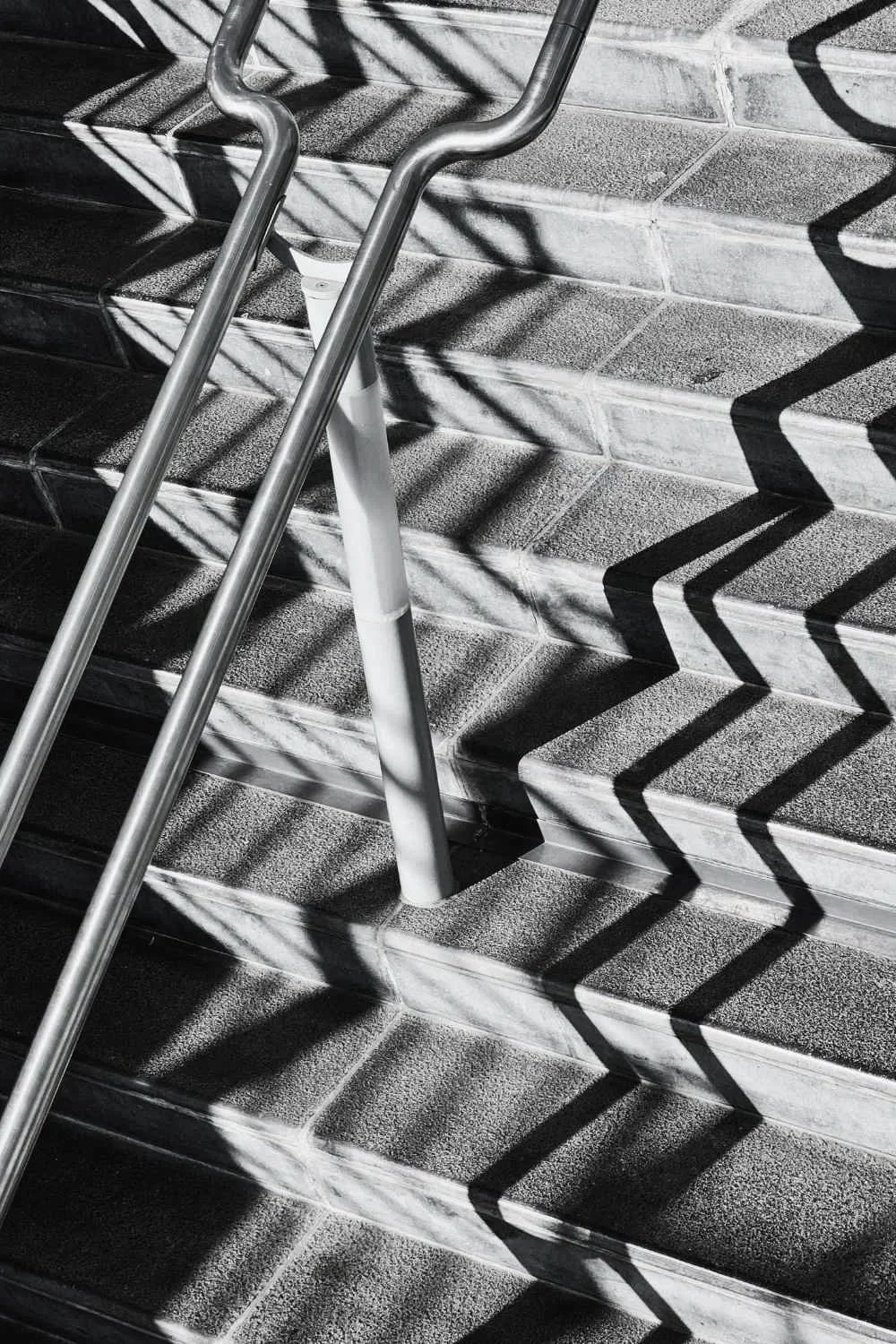 Black and white photo of stairs with shadows cast by a zigzag metal railing.
