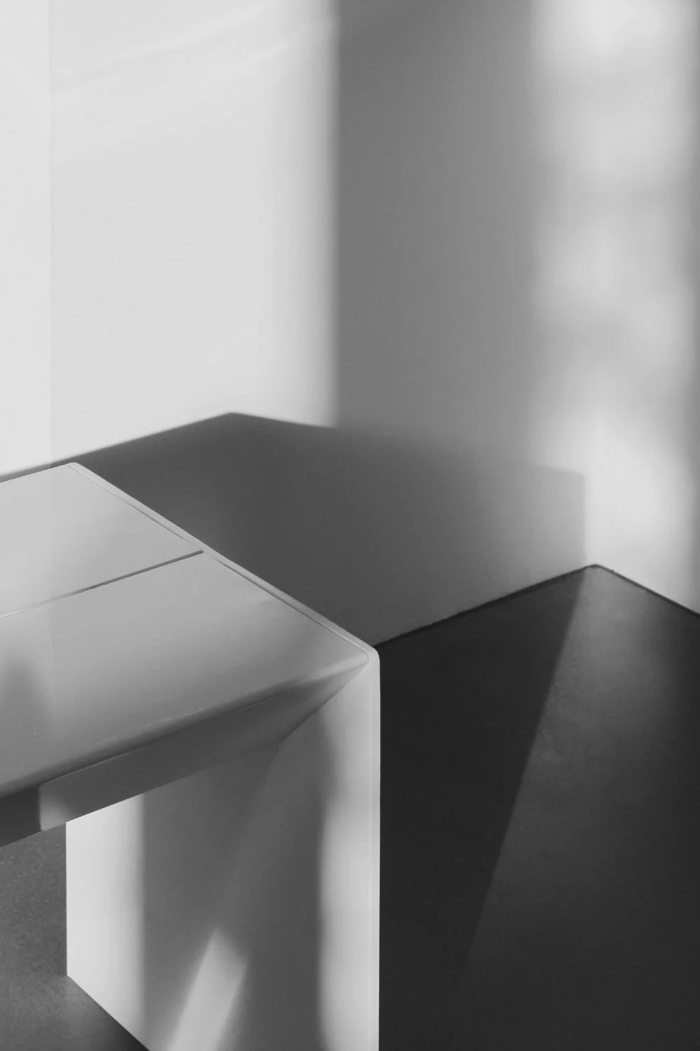 A corner of a white modern cabinet or printer with a smooth surface, with shadows cast on the wall behind it, creating distinct light and shadow areas.