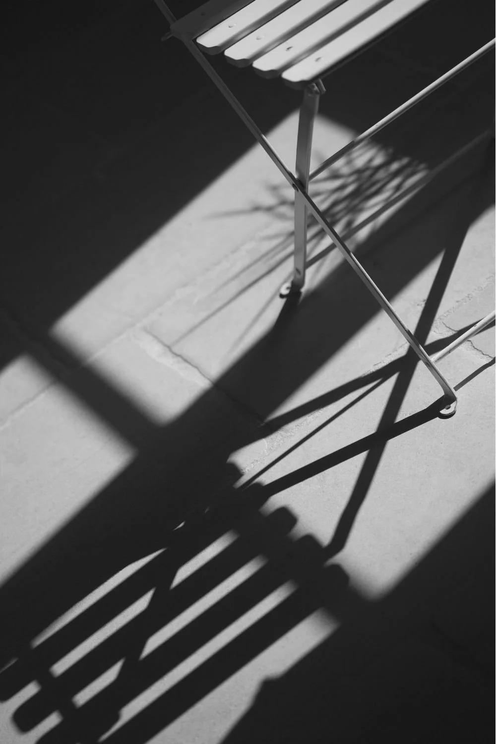 A metal chair on a tiled floor casting shadows in sunlight.