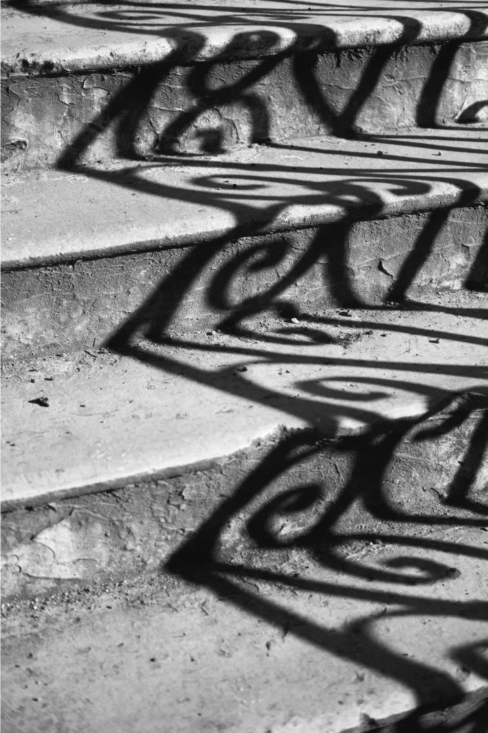 Shadow of a decorative curled metal railing cast on stone steps and ground.