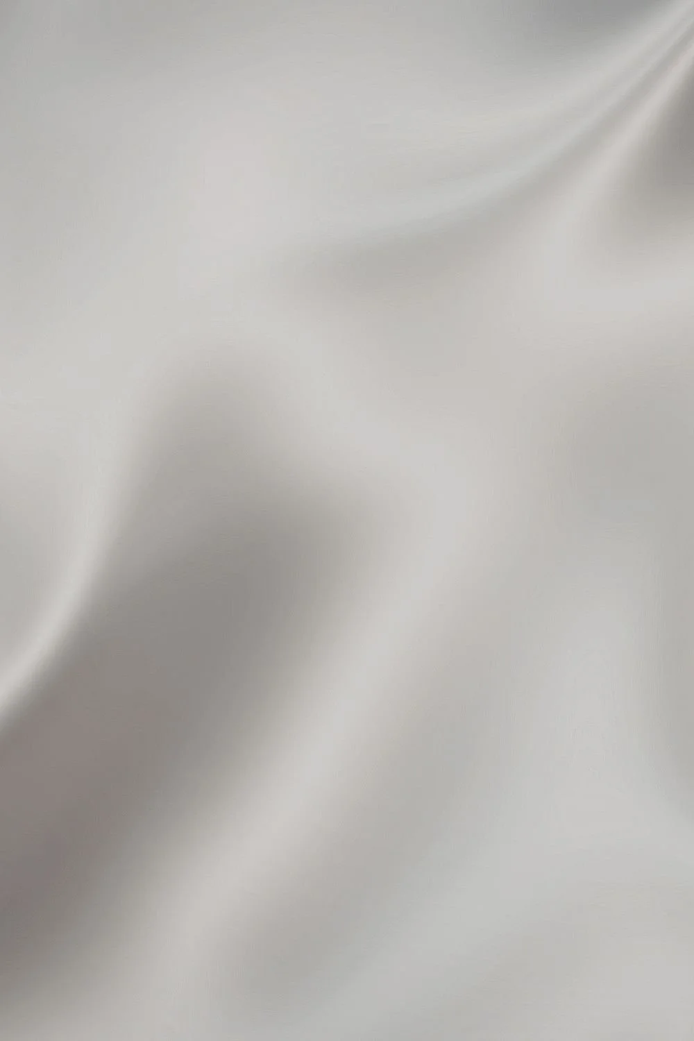 Close-up of smooth, light gray satin fabric with gentle folds and sheen.