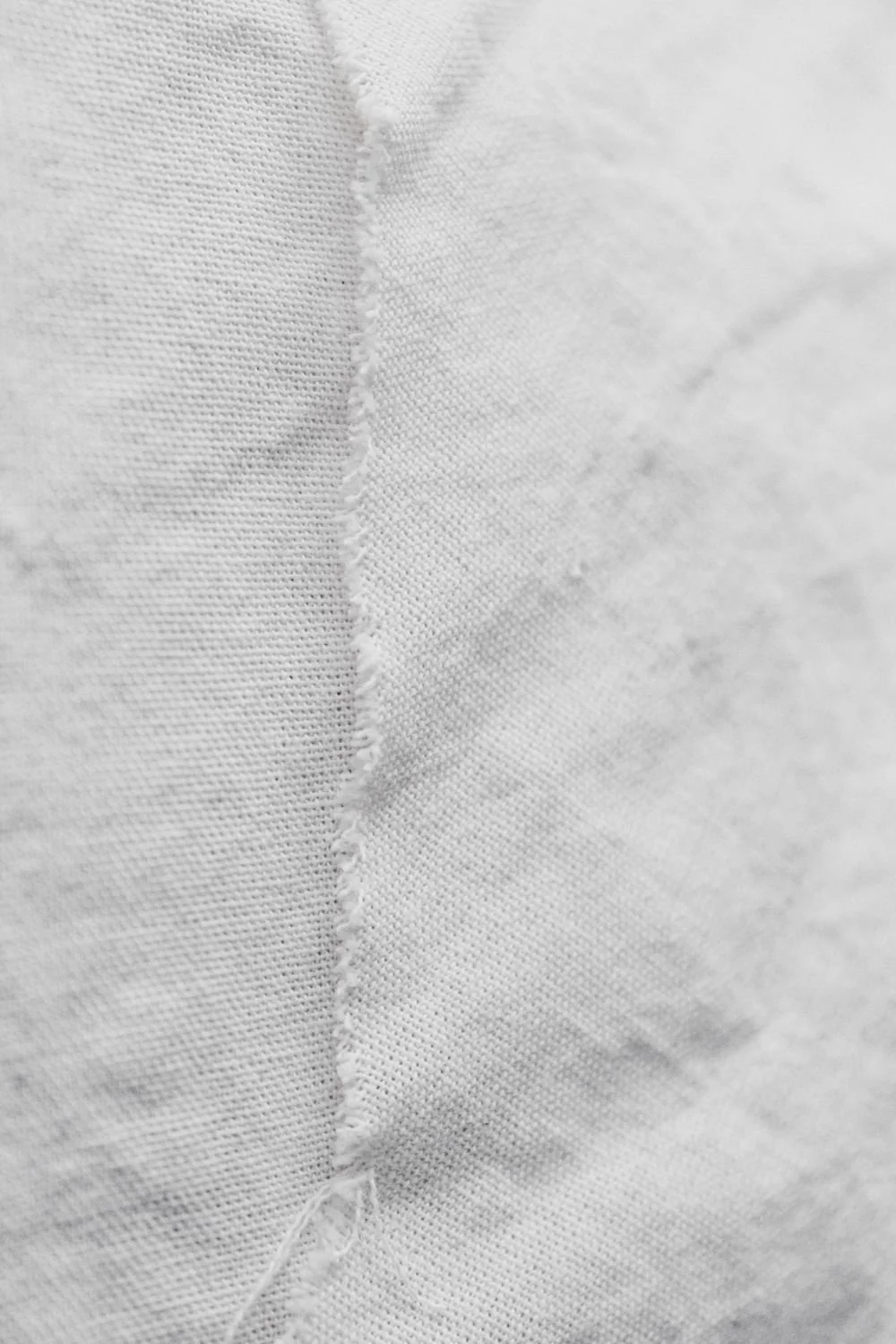 Close-up of white fabric with visible seam and frayed edge.