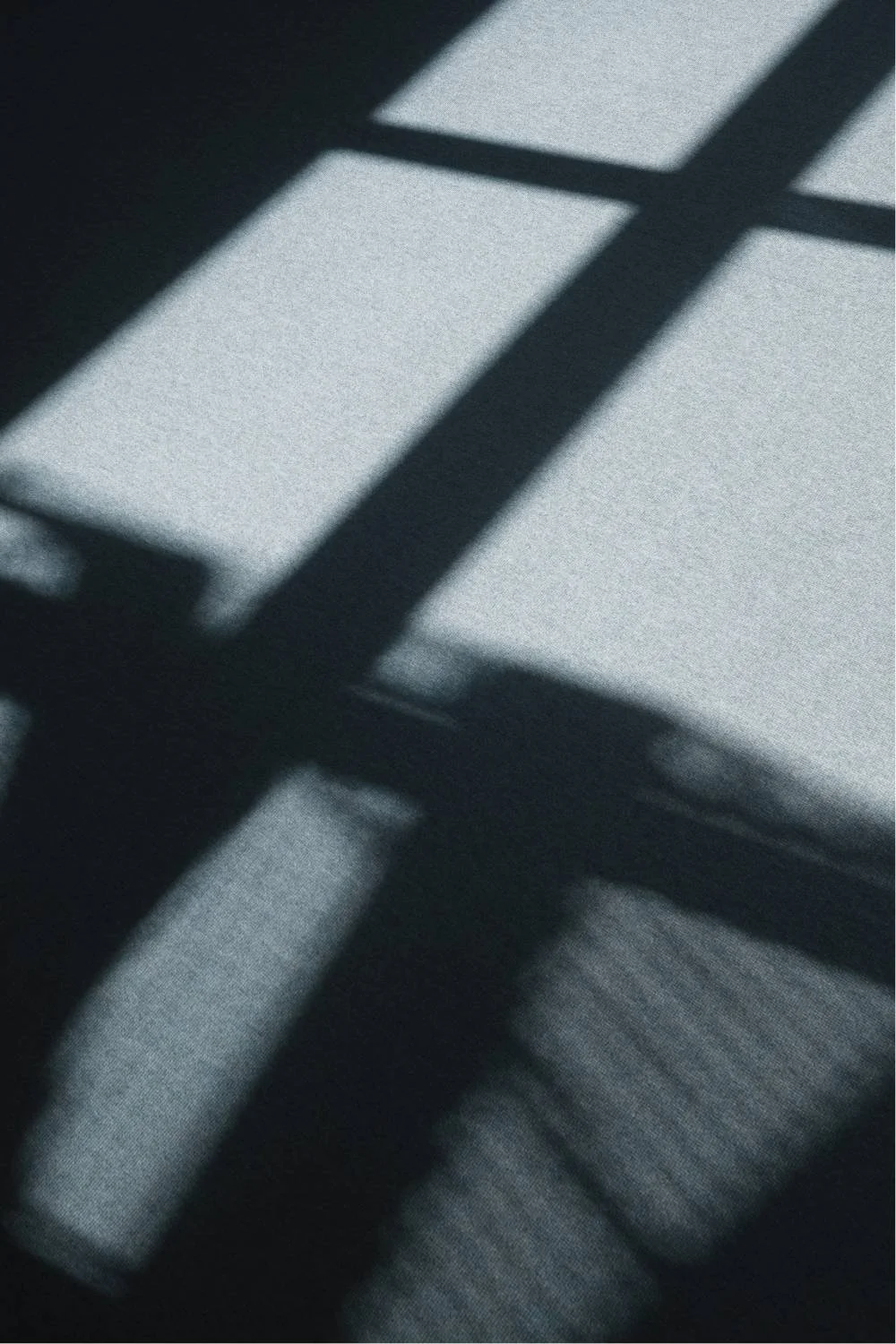 Shadows of a window frame cast on a gray fabric surface.