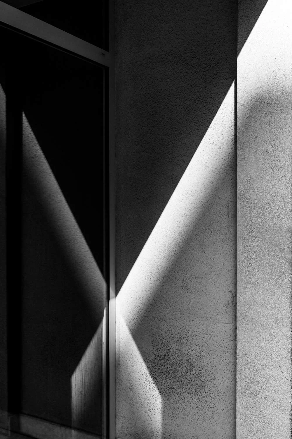 Black and white photograph of sunlight casting geometric shadows on a textured wall next to a window or door.