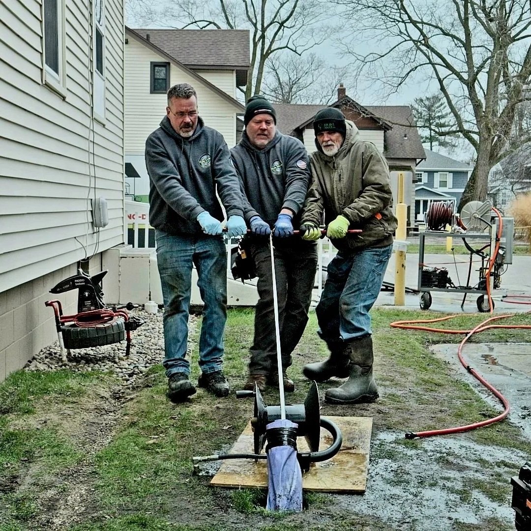 Plumbers clearing main sewer line blockage outside residential home.