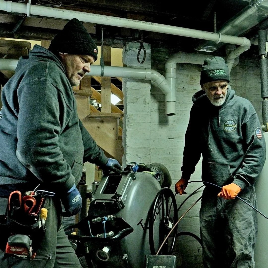 Plumbers inspecting basement floor drain system for main line blockage.