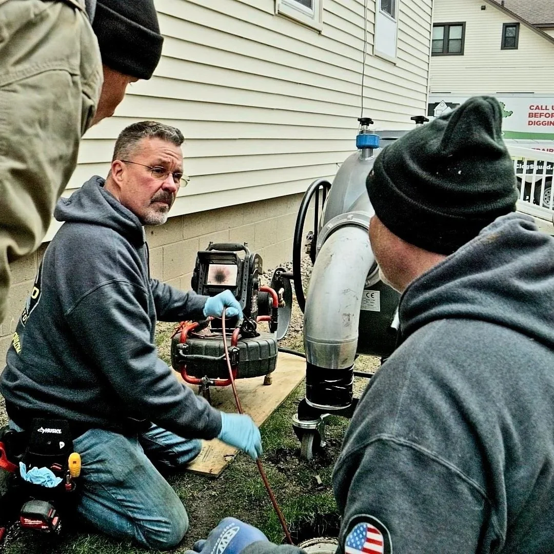 Technicians inspecting drain line equipment during outdoor sewer cleaning service.